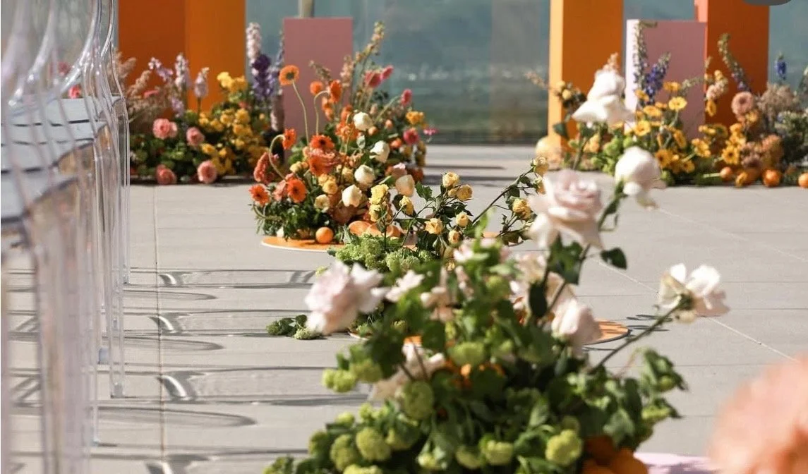 Sculptural floral arrangements lining an outdoor event aisle.