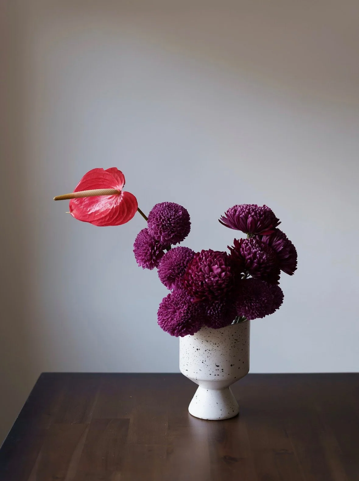 Red anthurium and deep burgundy flowers in a sculptural ceramic vase by Totem Flowers.
