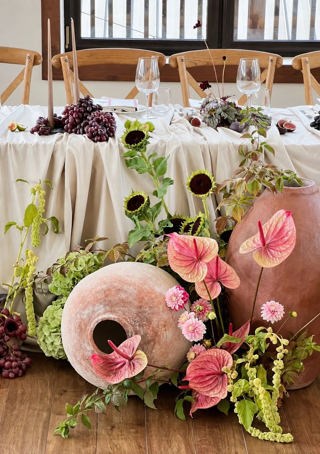 Sculptural pink anthuriums, green flowers and textured ceramic vessels beside a dining table dressed for a private event.