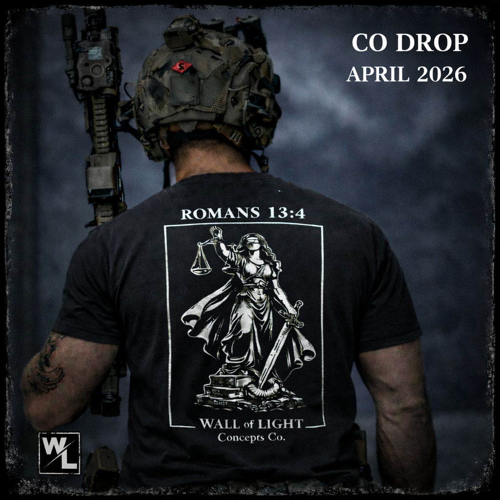 Back of a person wearing a black t-shirt with a graphic of Lady Justice and the text "Romans 13:4 WALL of LIGHT Concepts Co." The person is wearing tactical gear and a helmet with mounted equipment.