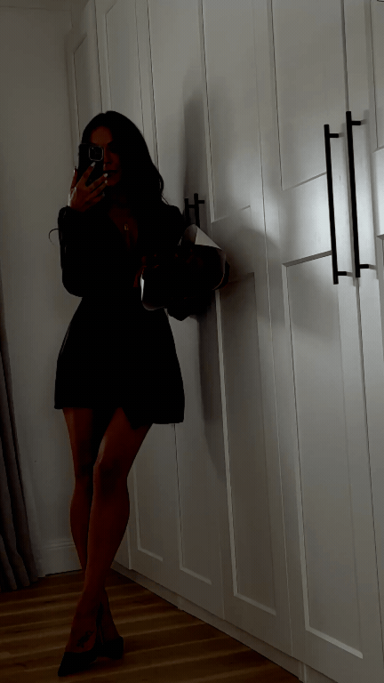 A woman taking a mirror selfie in a room with white paneled wardrobes, wearing a black dress and high heels. Love Letty Content, Luxury Wedding Content Creation in Dallas Texas.
