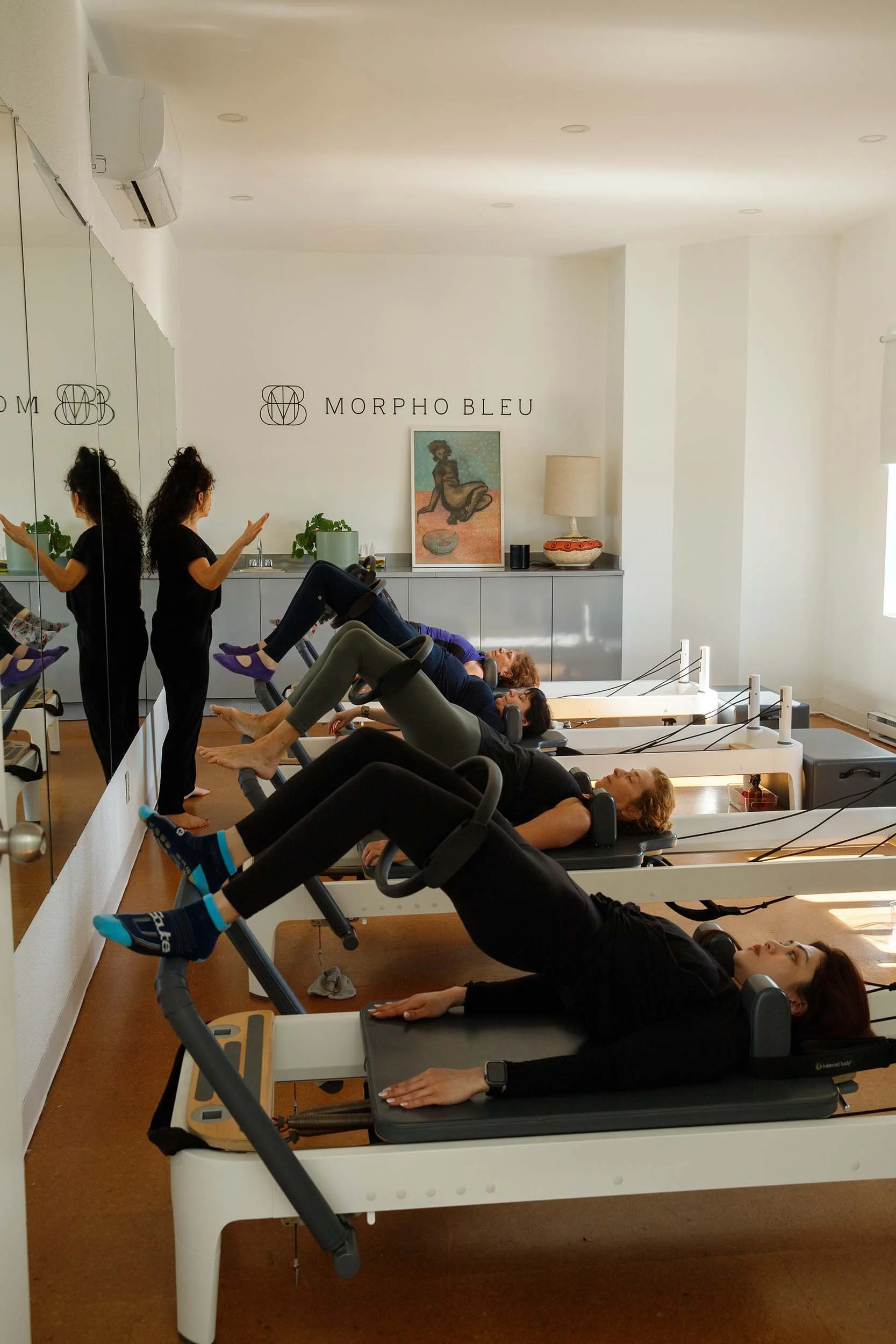 One teacher and four students doing reformer pilates in a cozy studio