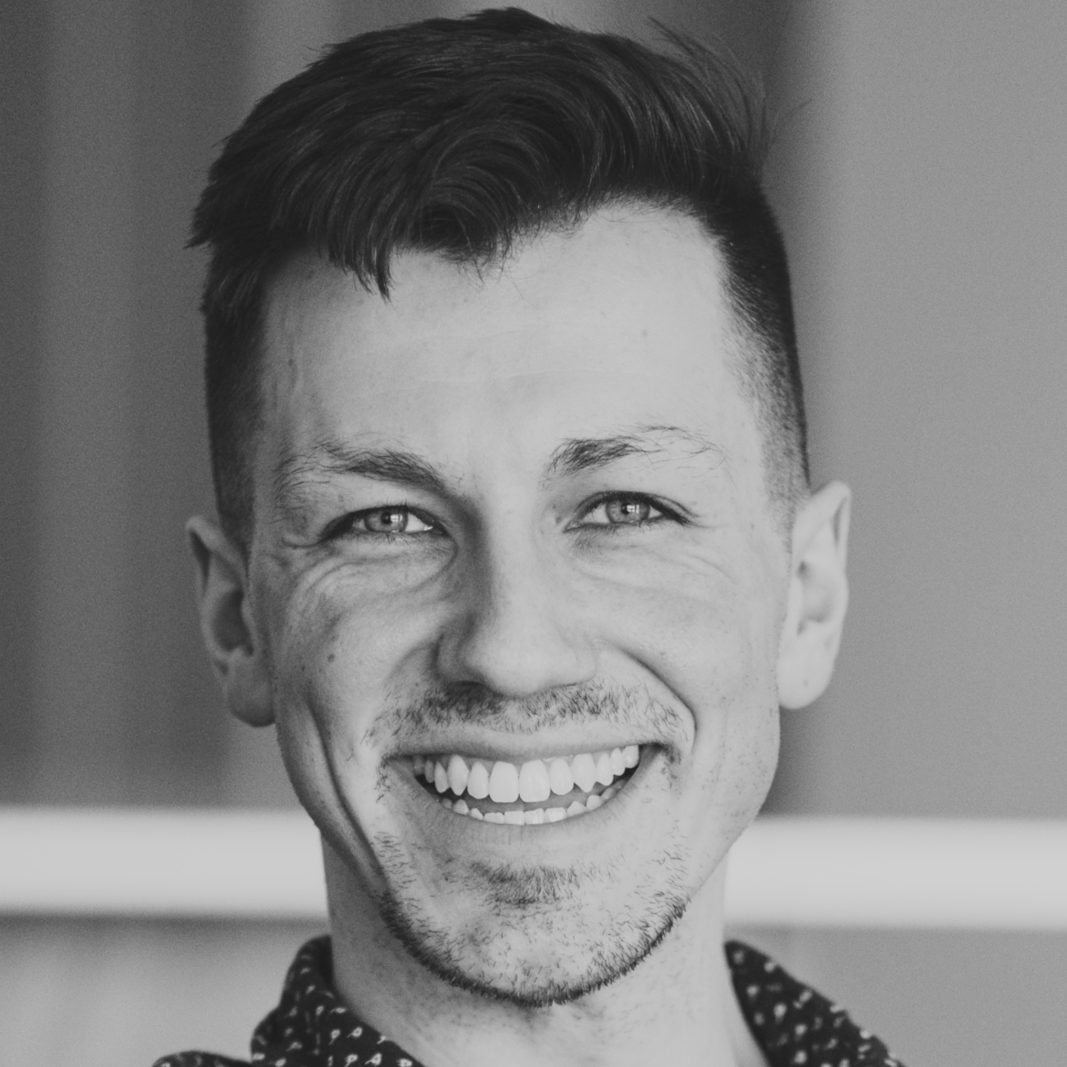 Black and white photo of a smiling young person with short dark hair, light skin, and wearing a polka dot shirt.
