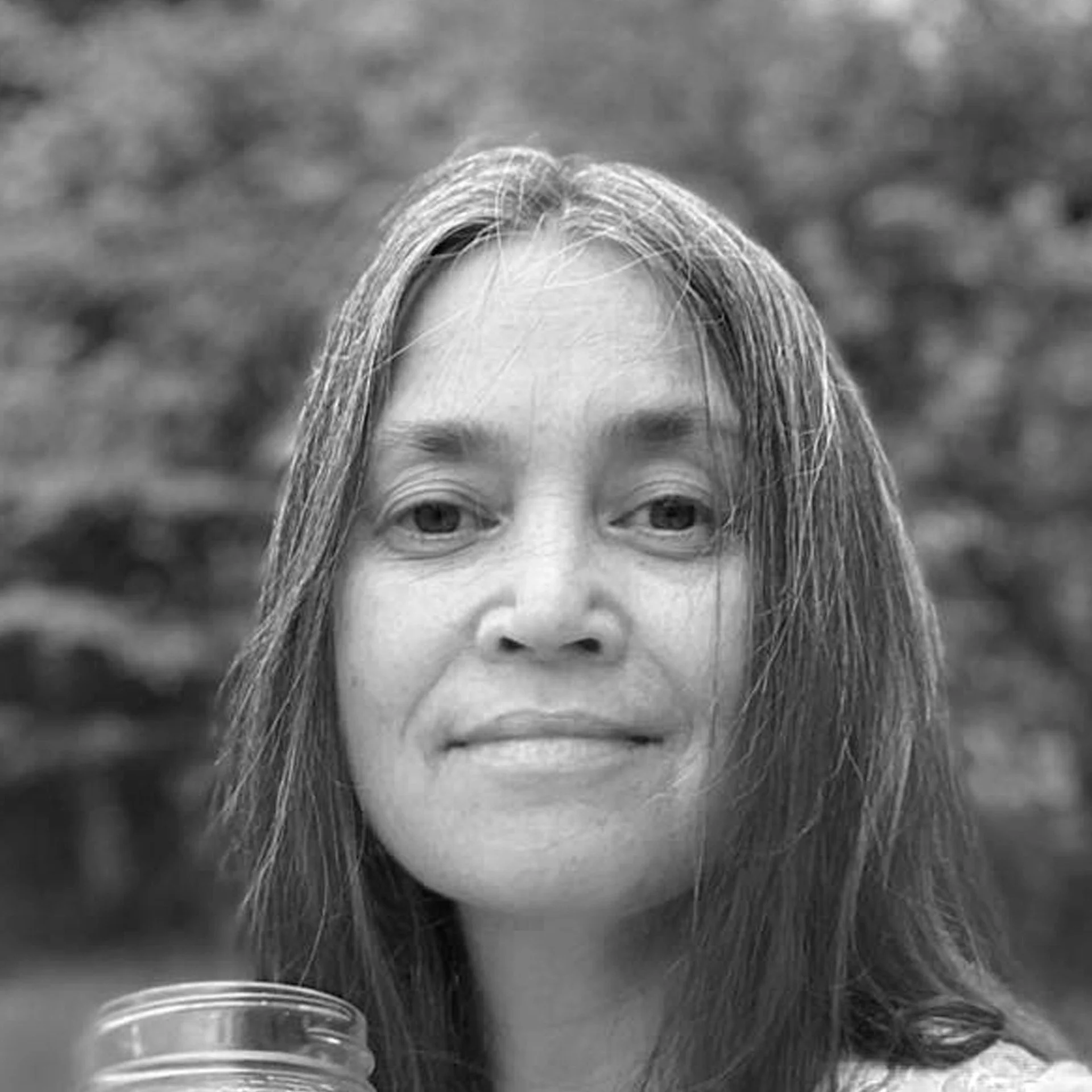 Close-up of a woman's face with long hair, outdoors with a blurred natural background.