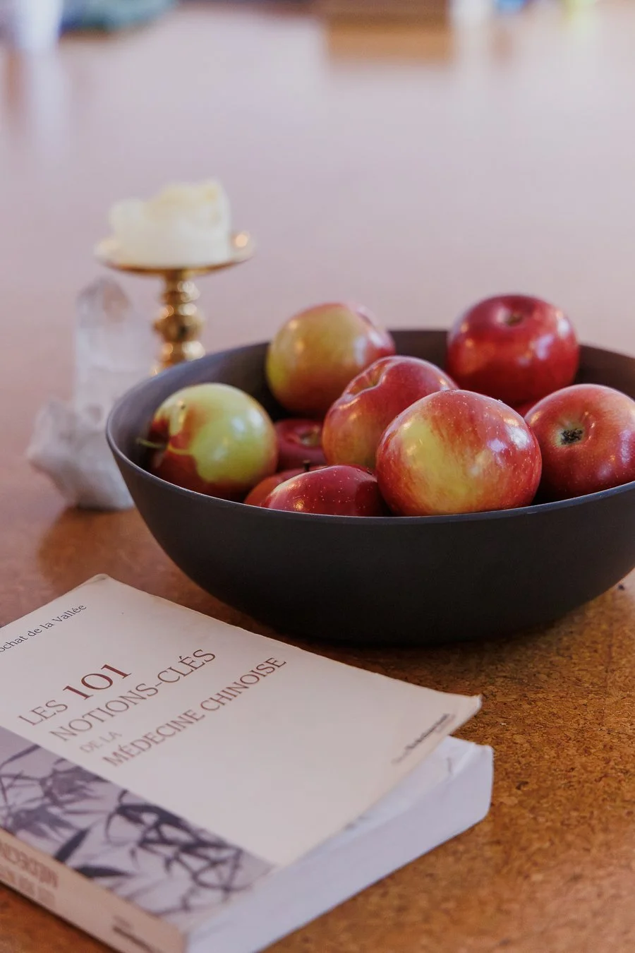 A bowl of apples beside a candle and a book on Traditional Chinese Medicine