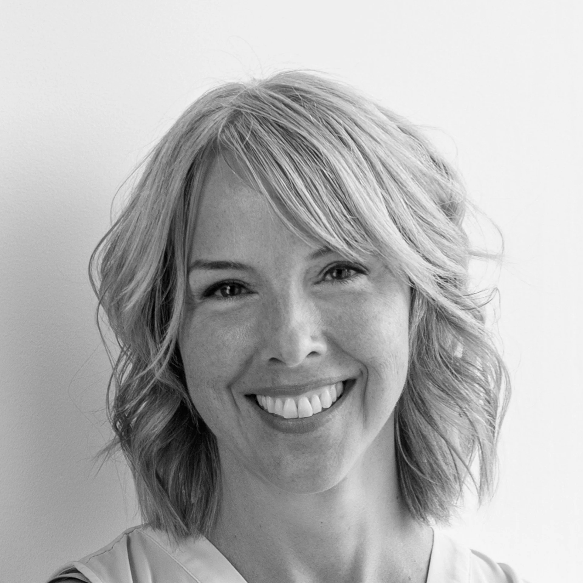 Black and white close-up photo of a smiling woman with blonde hair, showing her face from the forehead to the shoulders, against a plain background.