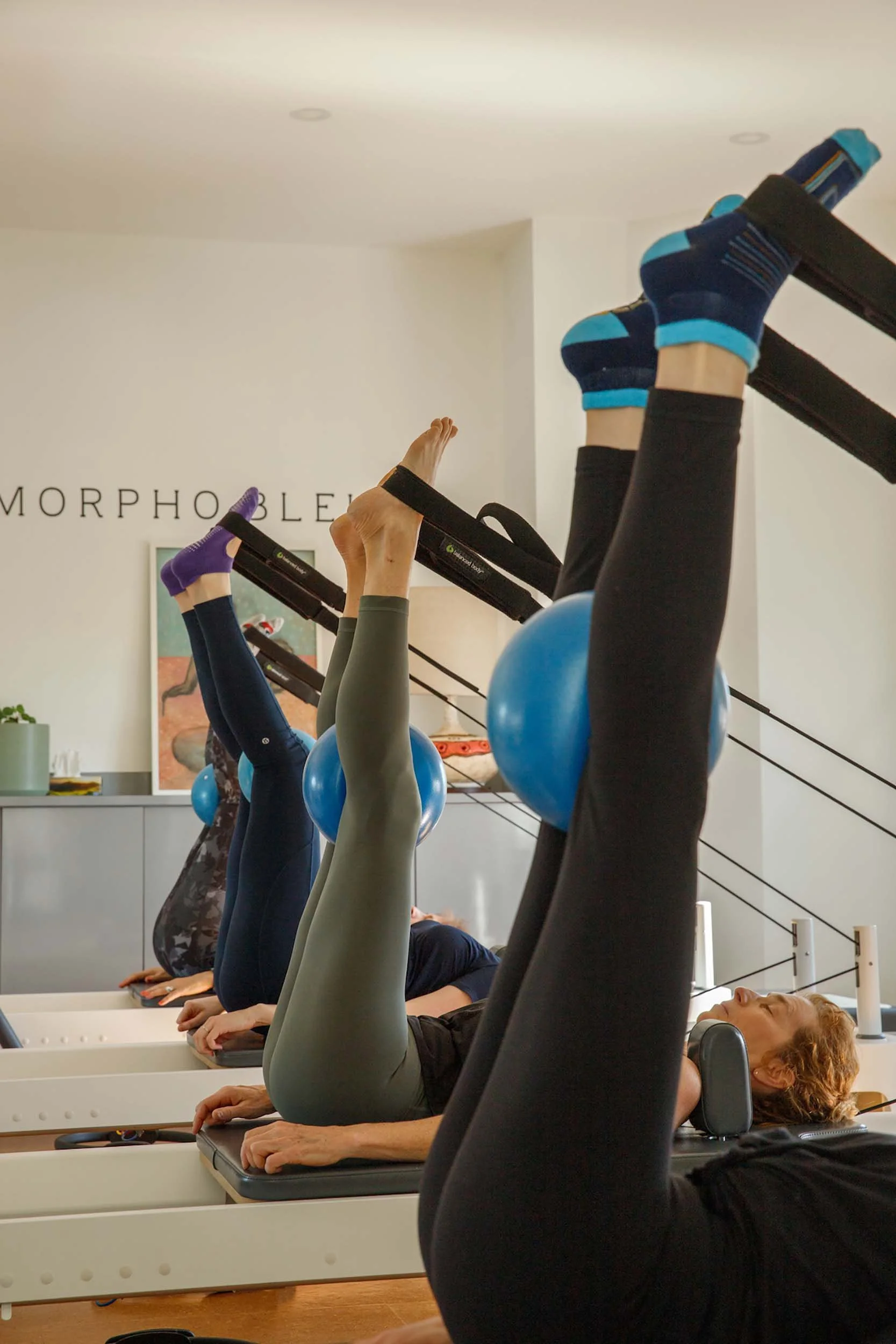 Students doing reformer pilates with legs up in straps