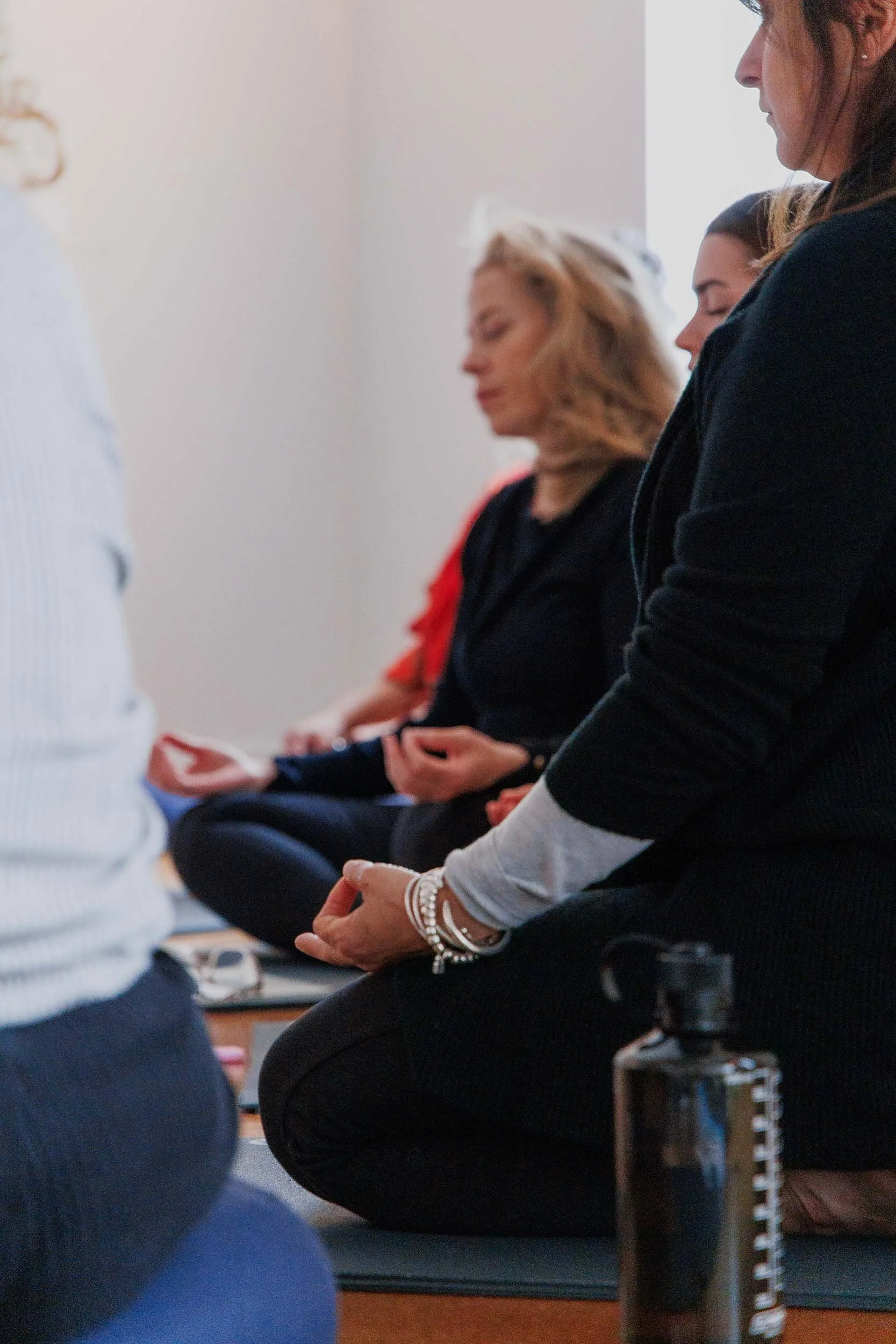 People sitting on a yoga or meditation mat, with their eyes closed and hands resting on their laps, practicing meditation or mindfulness indoors.