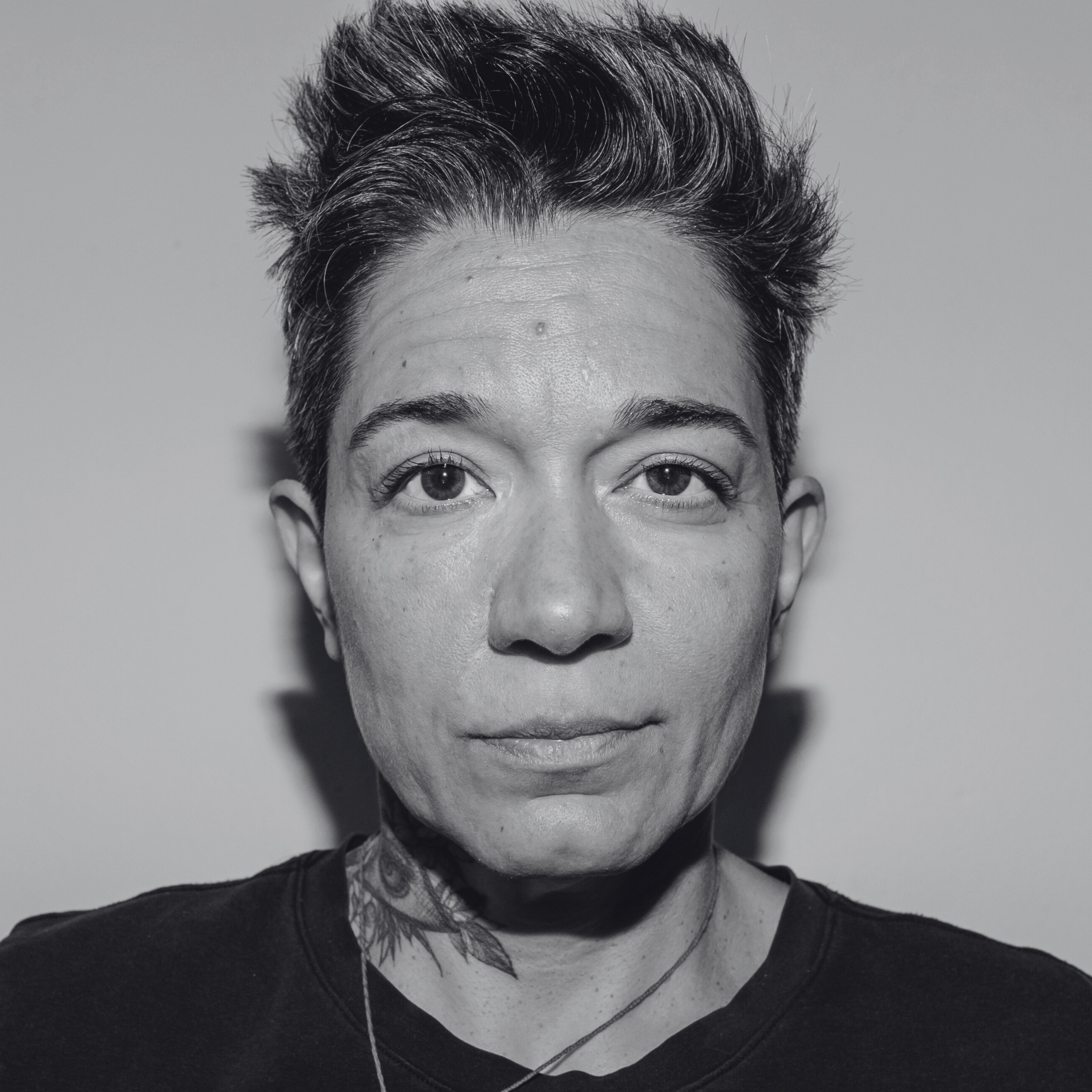 Close-up black-and-white photo of a person's face, showing their forehead, eyes, and part of their nose and mouth, with short, styled hair and a dark shirt.