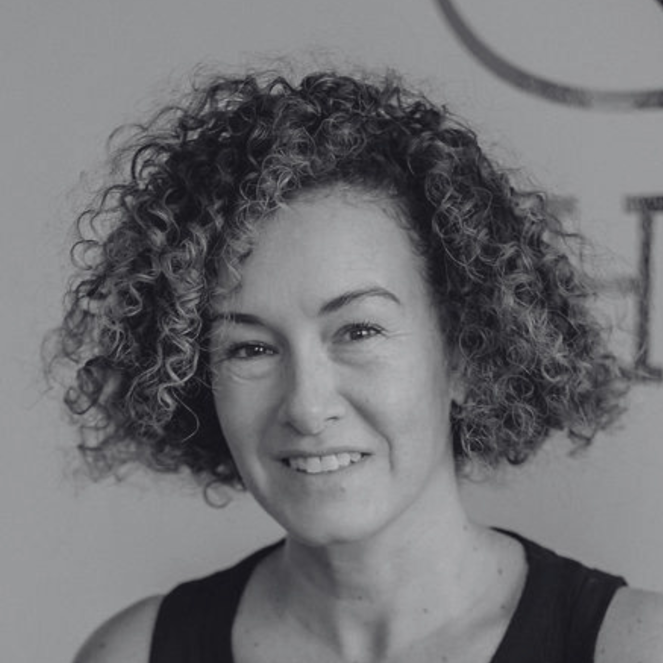Close-up of a woman with curly hair smiling, taken from above, with part of her face and hair visible.