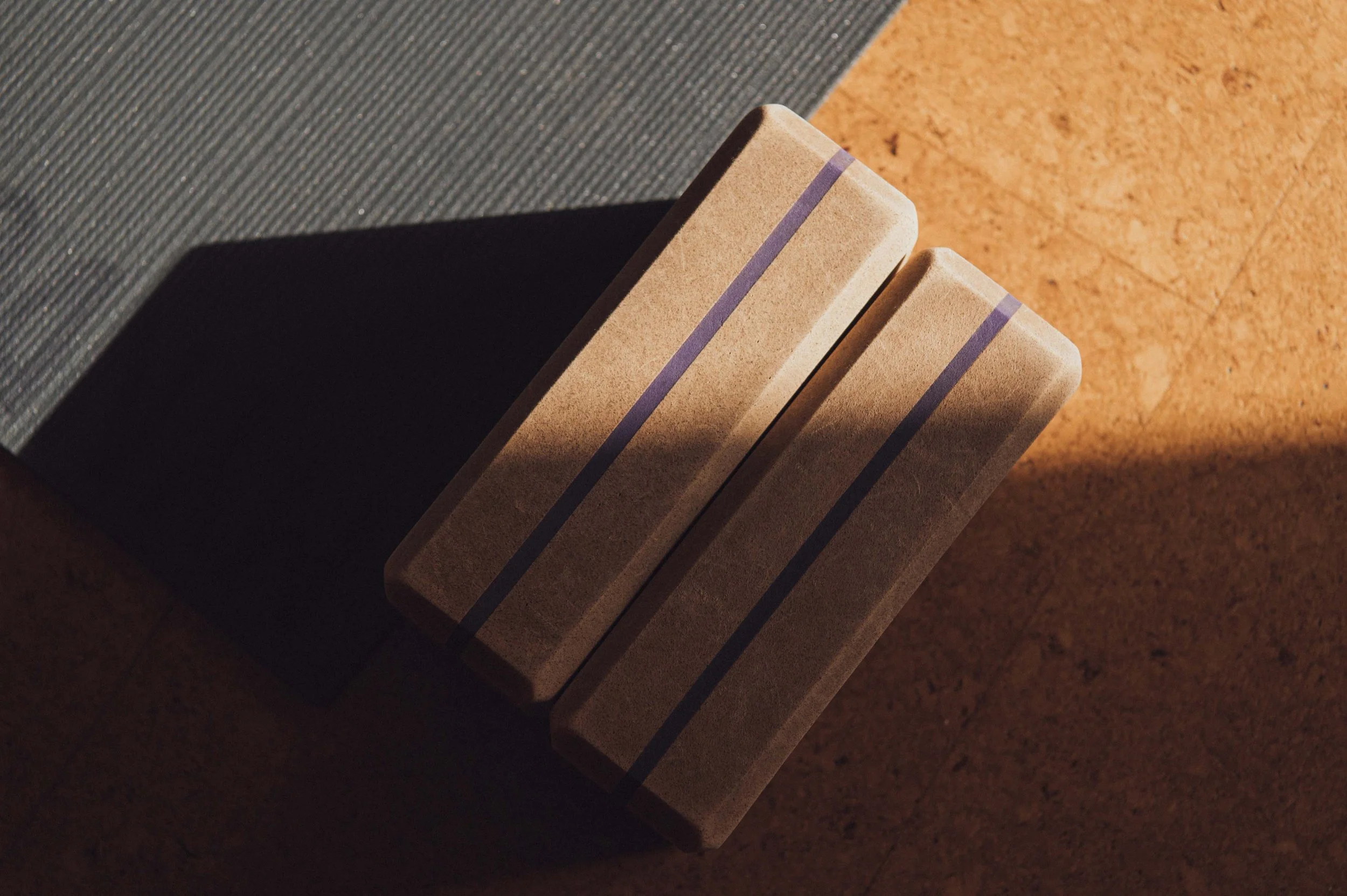 Two yoga blocks and a yoga mat on a cork floor in the sunlight