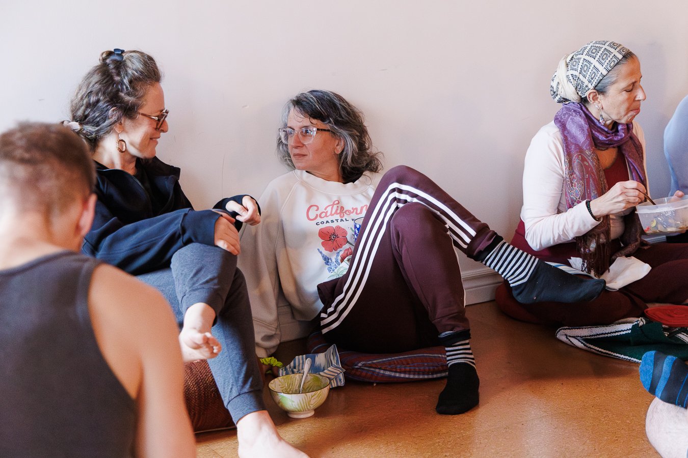 Students chatting on meditation cushions in a yoga studio
