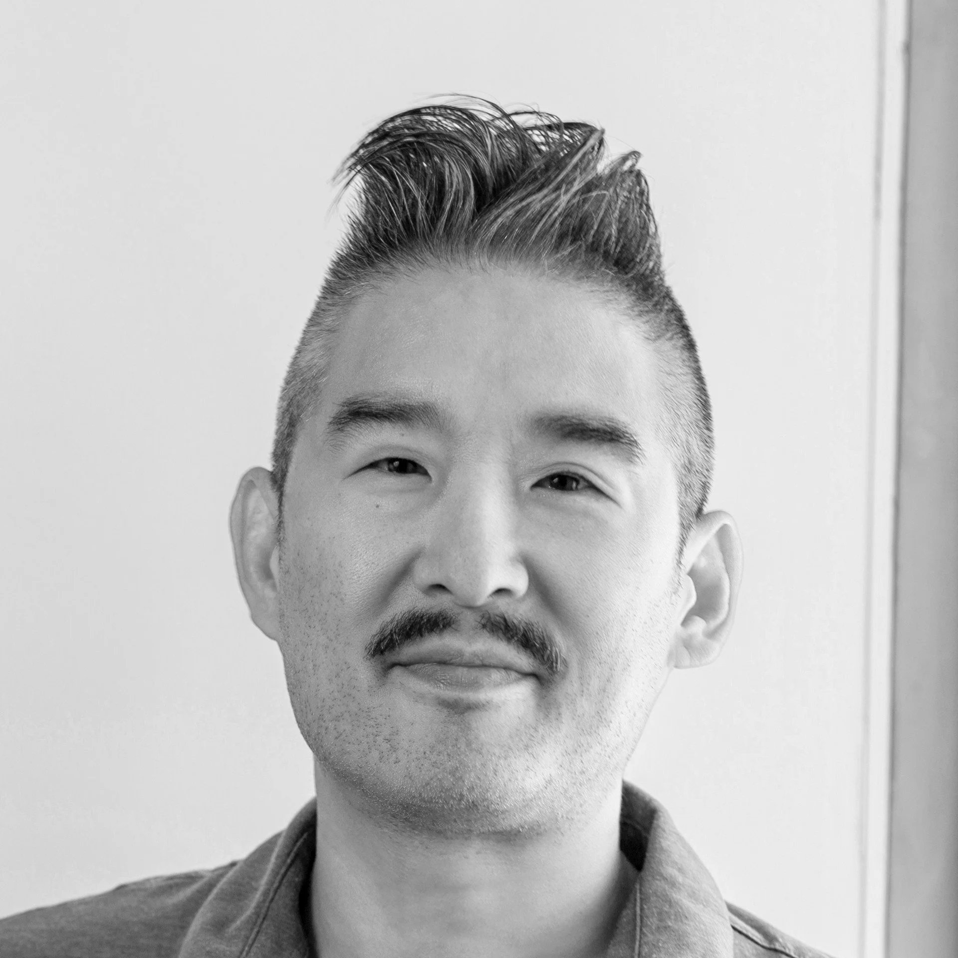 Black and white photo of a young man with short, styled hair, smiling slightly, wearing a collared shirt.