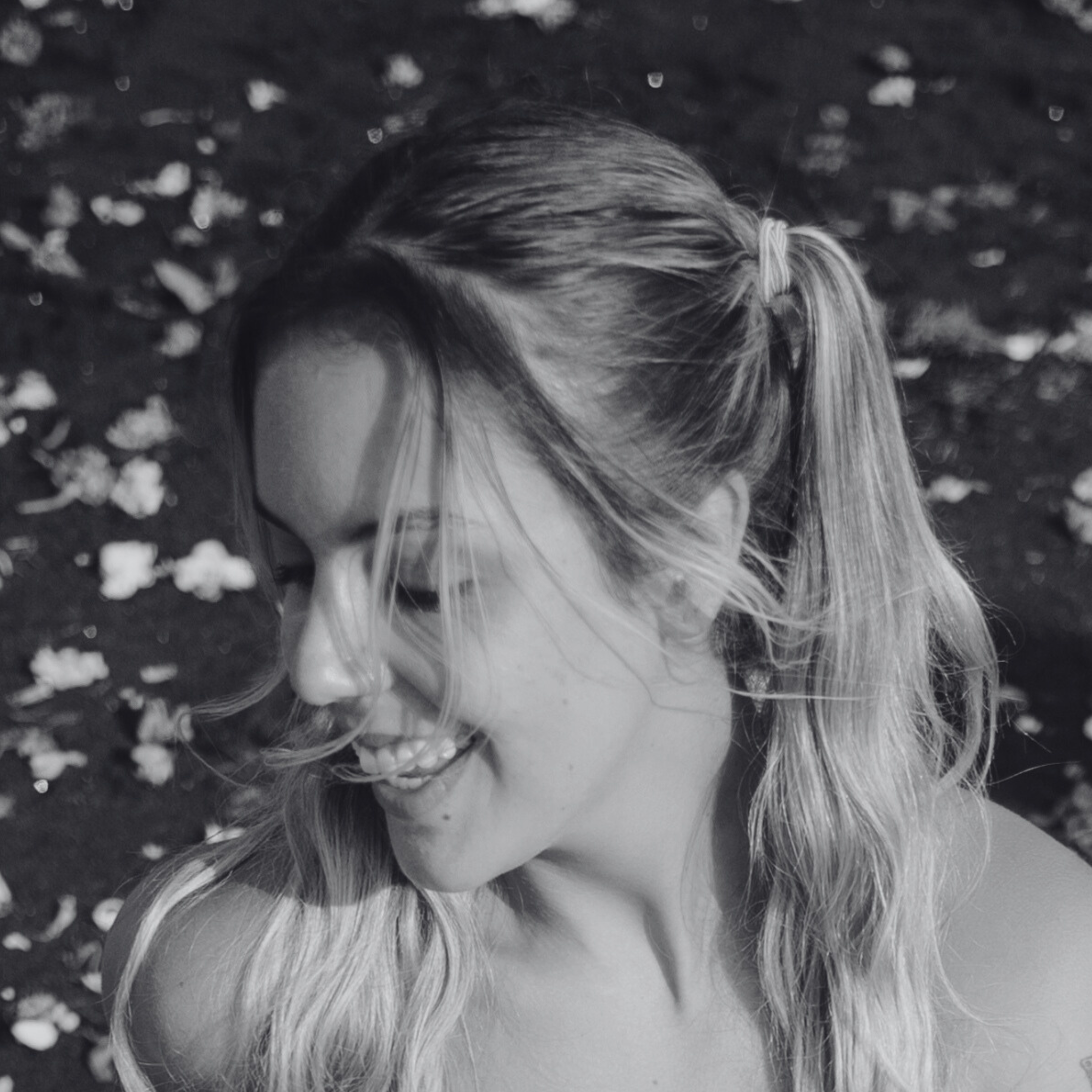 Close-up of a child's head with blonde hair tied in a ponytail, lying on the ground among scattered small rocks or pebbles.