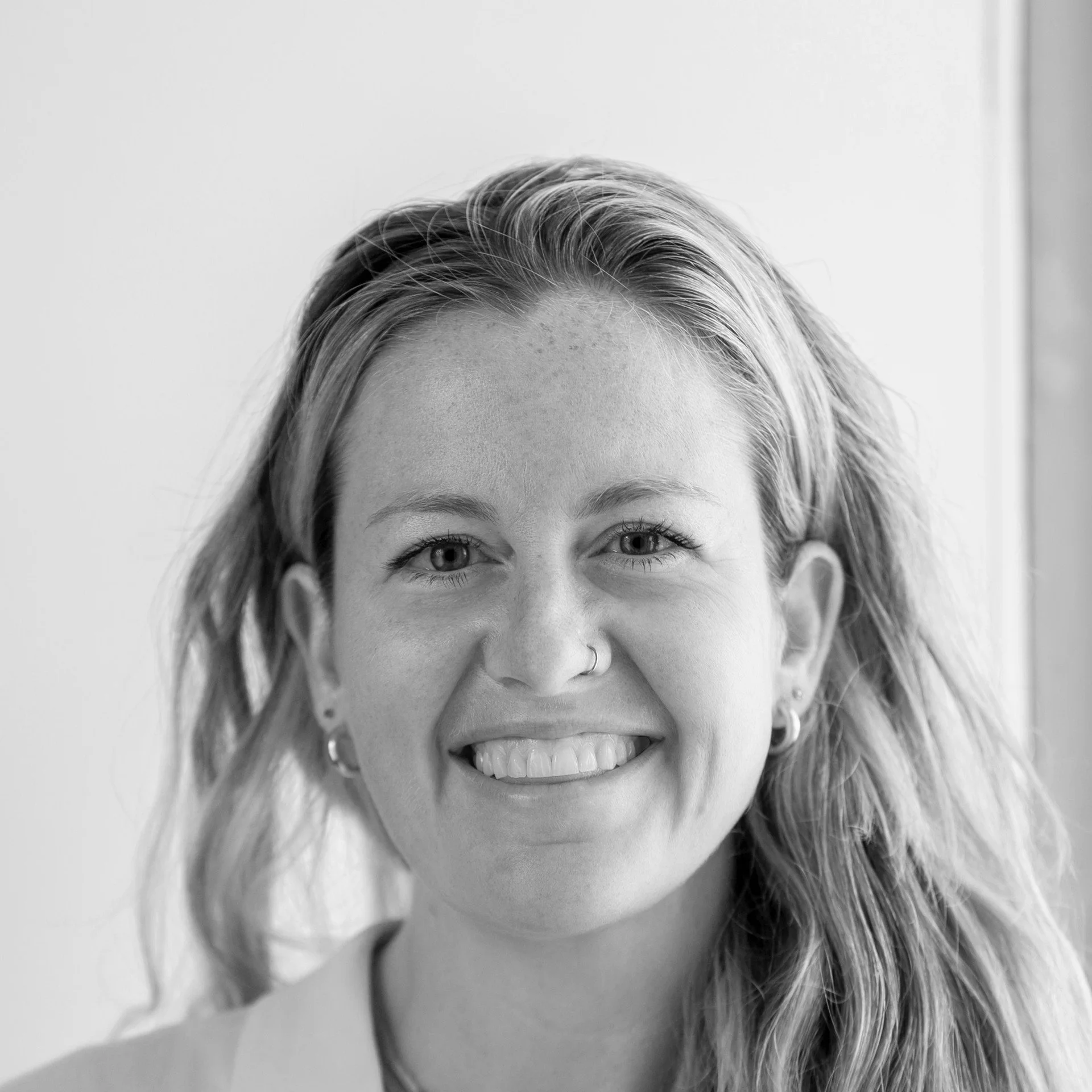 Black and white close-up photo of a woman smiling, shows her forehead, eyes, nose, and lips with braces, hair, and earrings.