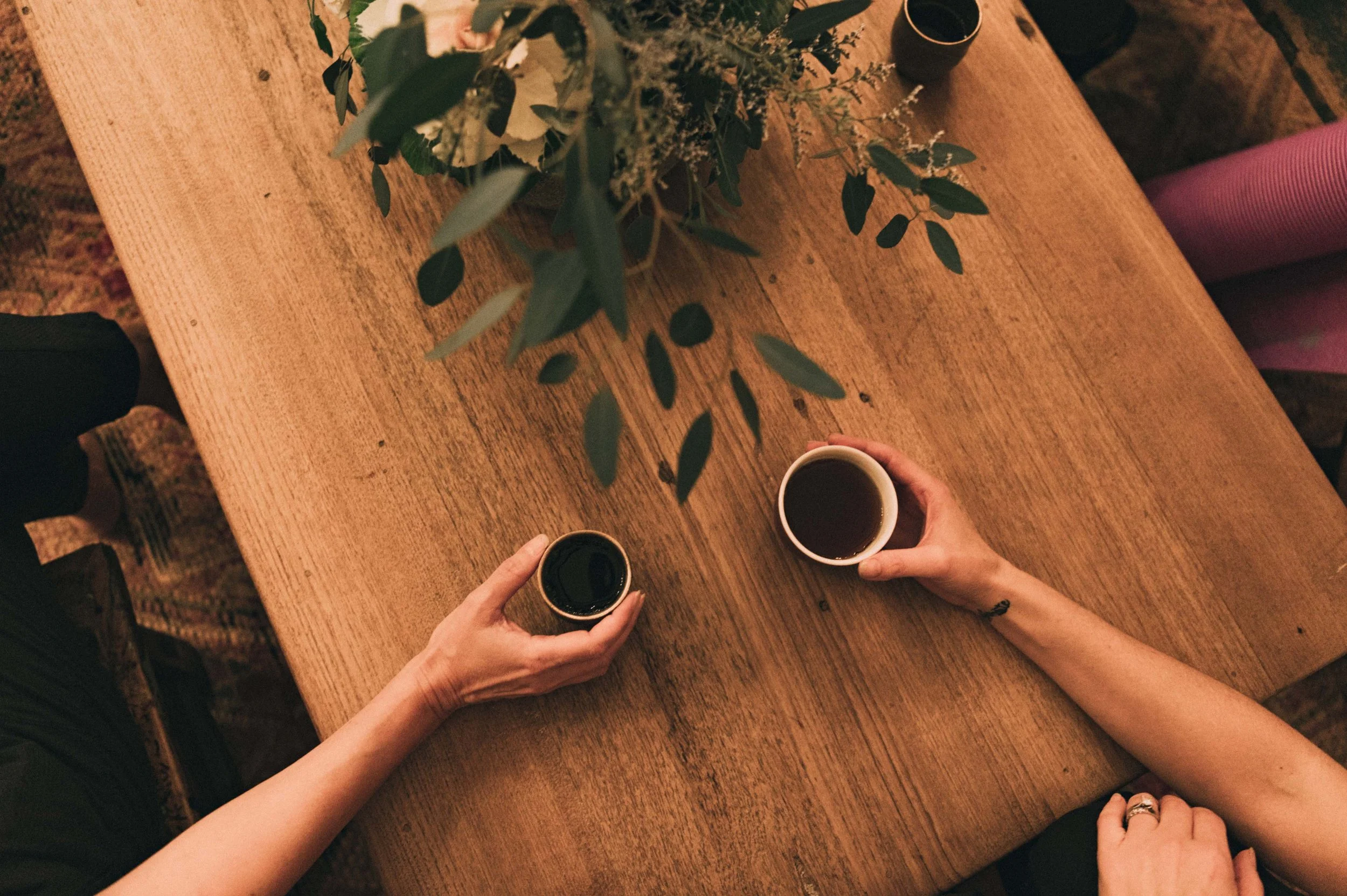 Two hands holding cups of tea on a vintage table with a plant