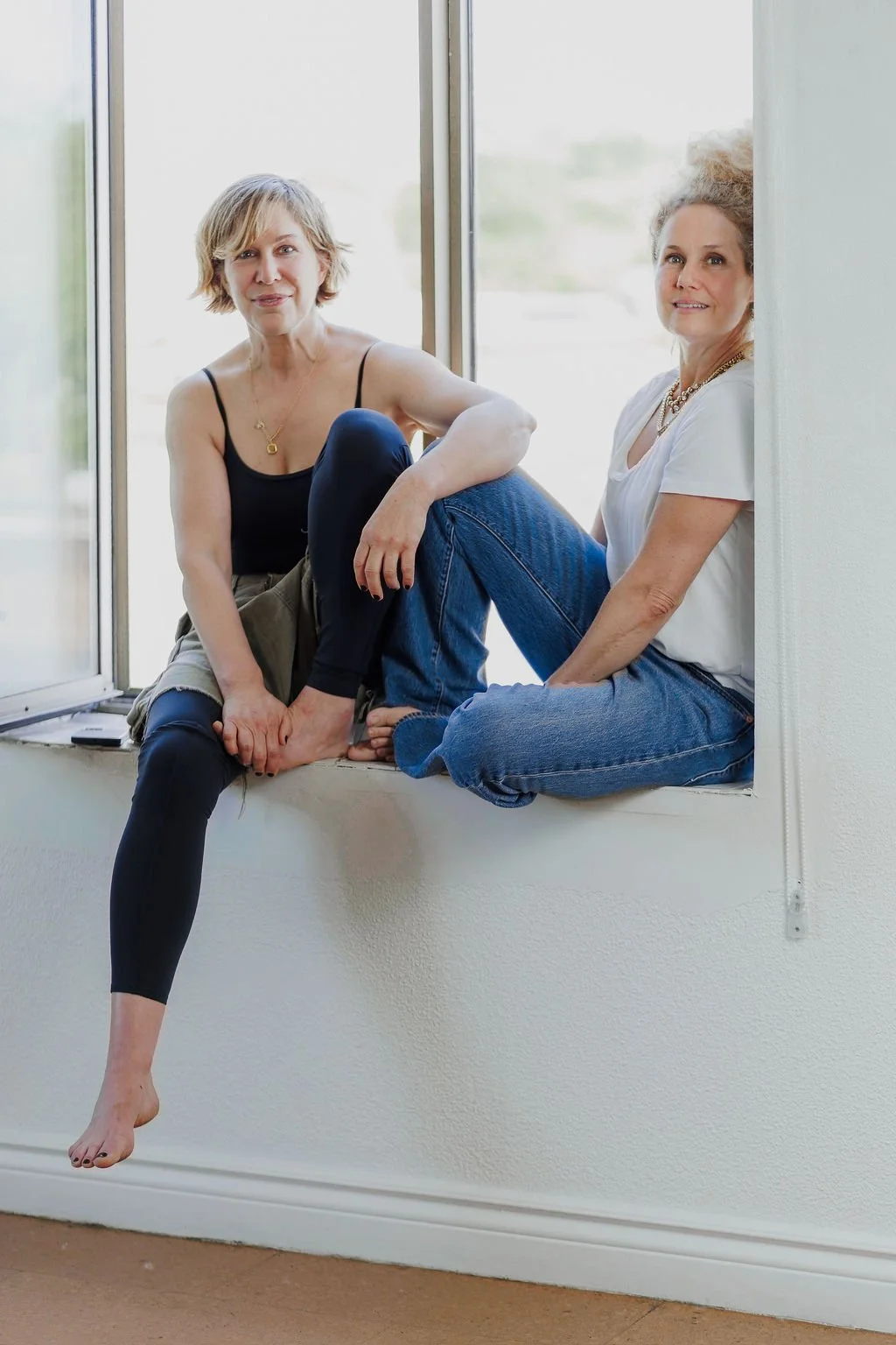 Studio Morpho Bleu co-owners, Sara and Kelly, sitting together in the windowsill of a sunny room.