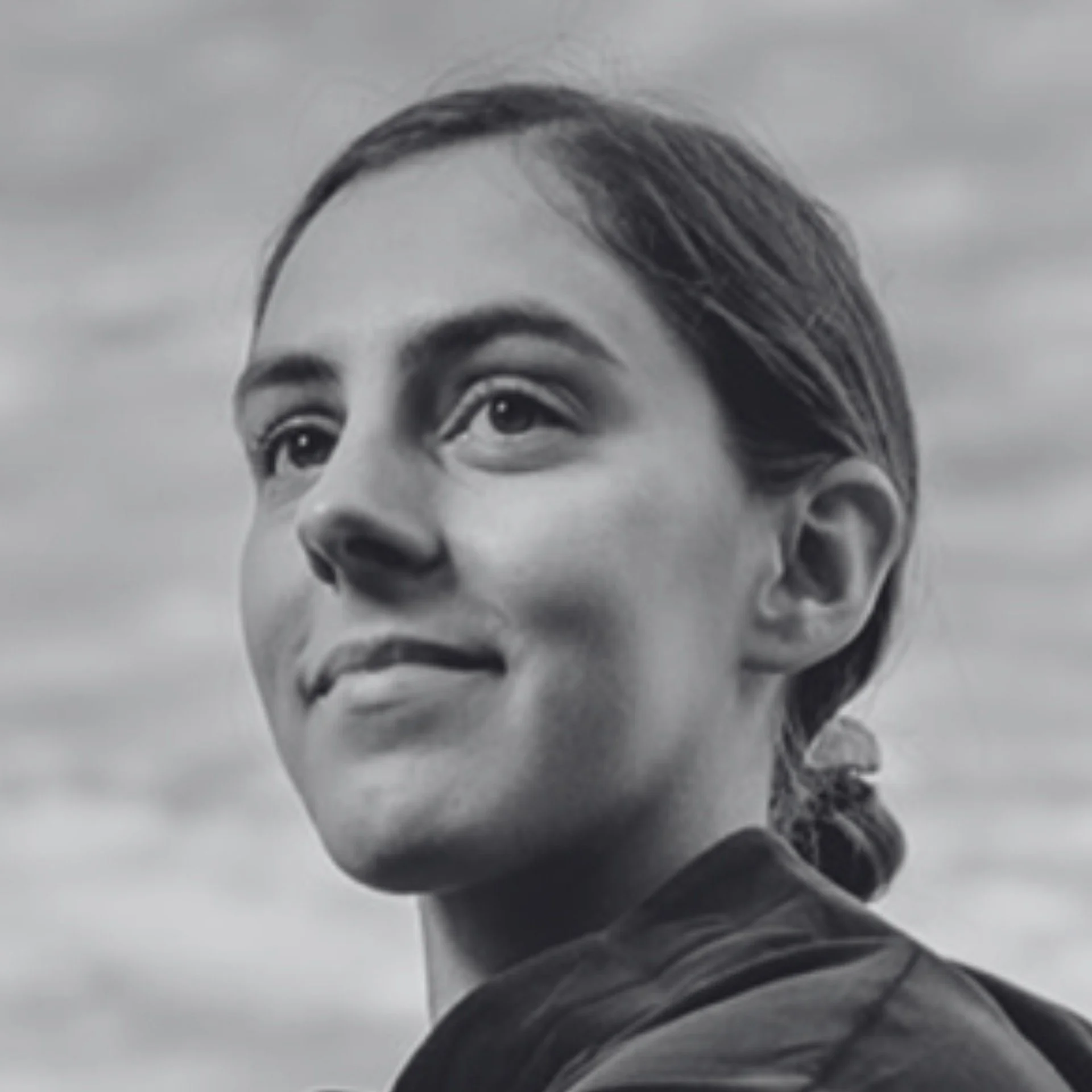 Close-up black-and-white photo of a person's face, shown in profile with a focus on their eye, eyebrow, and part of their hair. The person appears to be gazing upwards.