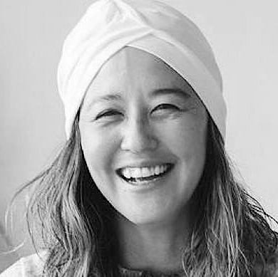 A smiling woman wearing a white head wrap in black and white photograph.