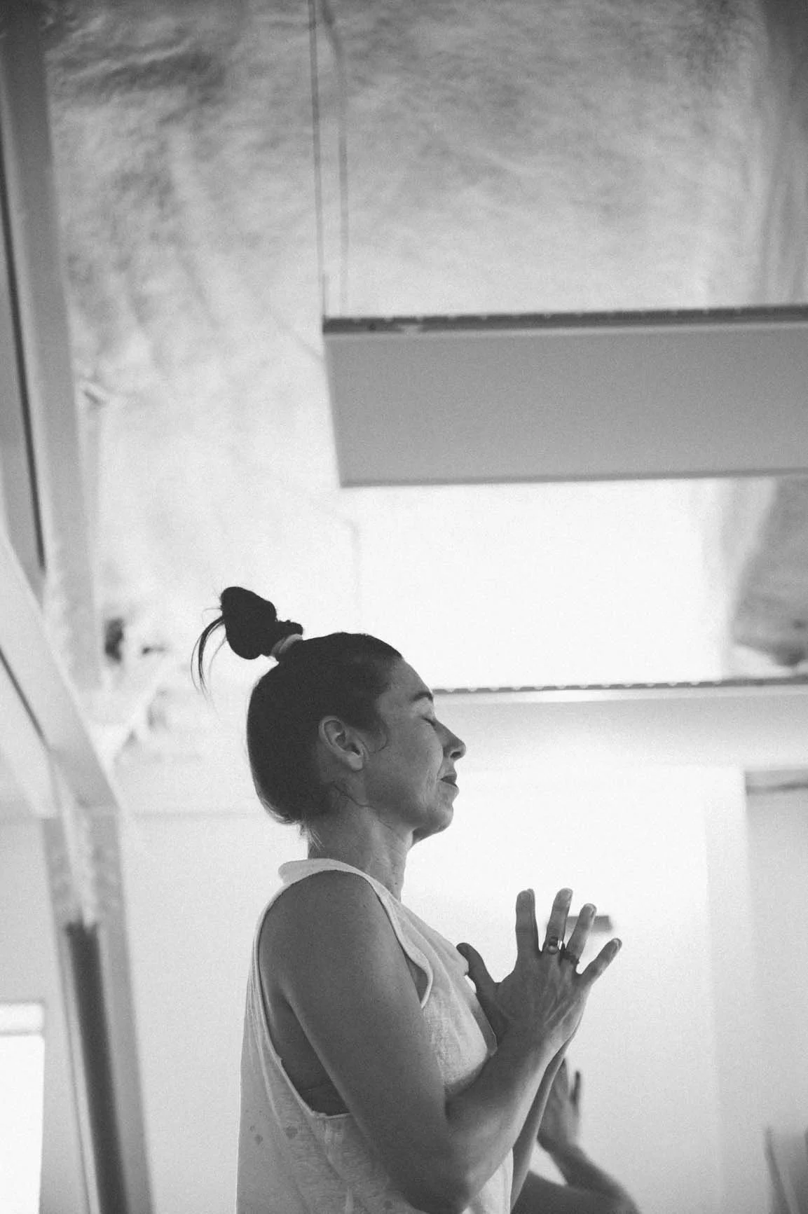 A woman's side profile with eyes closed and hands at her chest in prayer