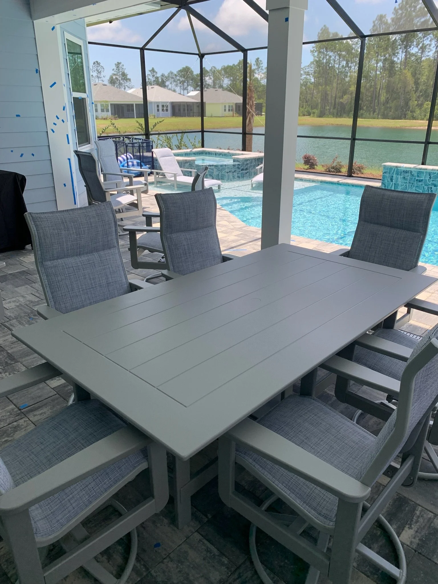 View of an outdoor screened patio overlooking a lake, featuring a dining table with chairs, a hot tub, and lounge chairs.