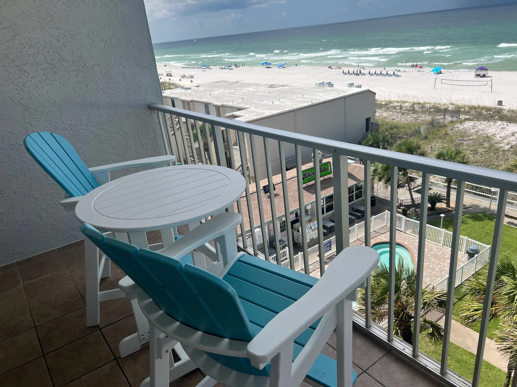 View from a balcony showing a beach with colorful umbrellas, lounge chairs, and the ocean in the background.