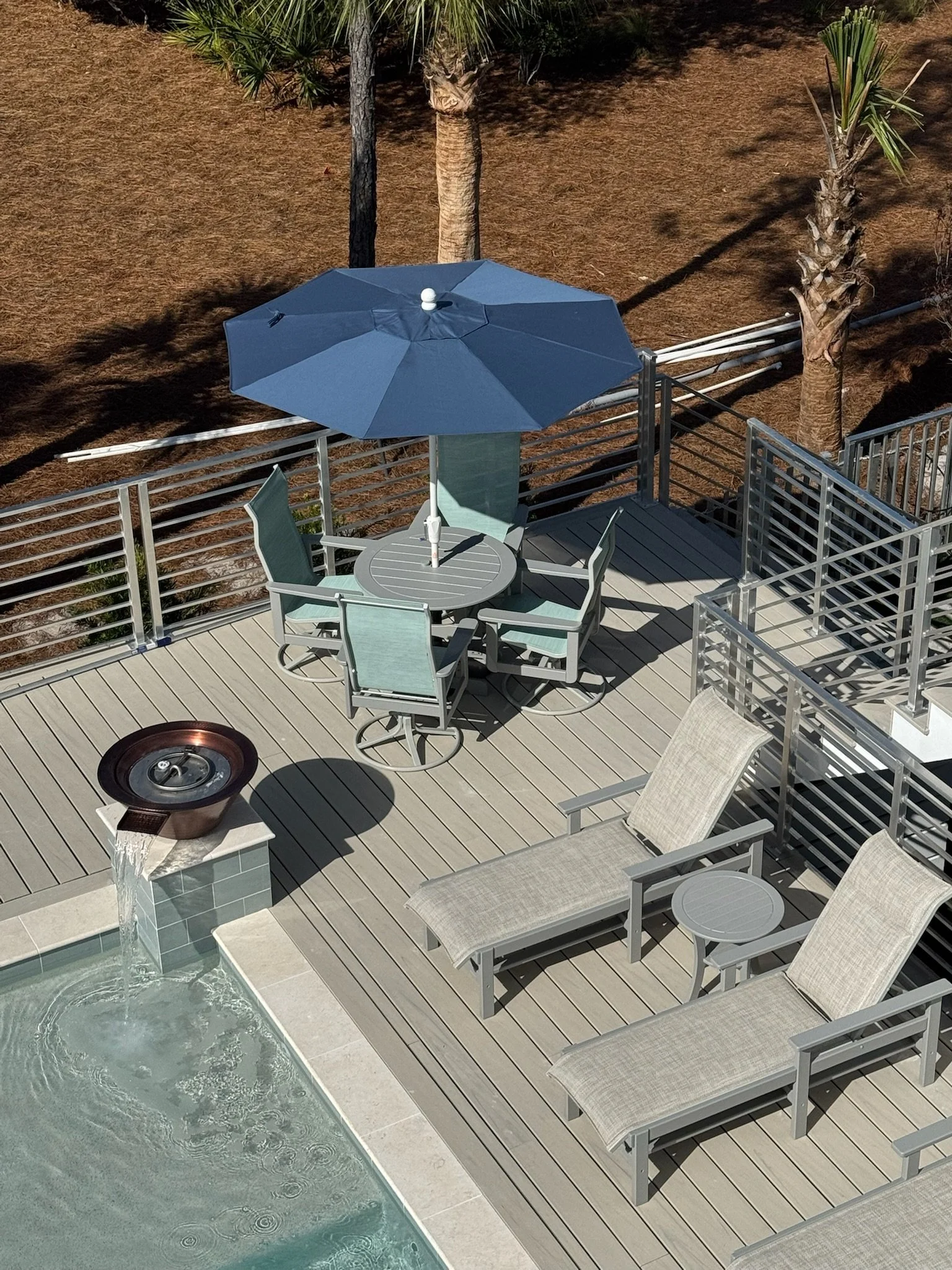 An outdoor patio area with a pool, beige chaise lounges, and a table with an umbrella.