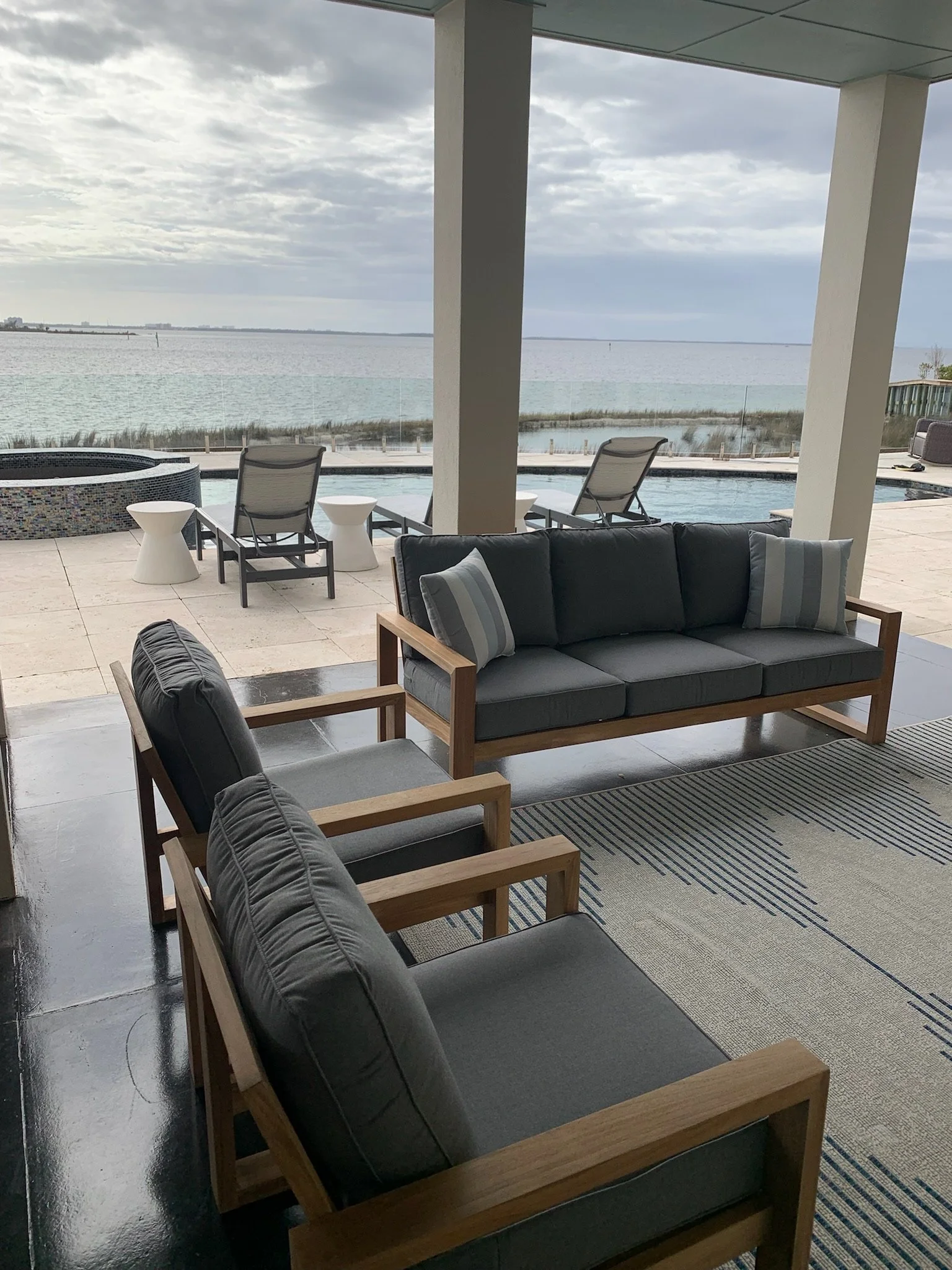 View of a living room with a black sofa, armchair, and a view of a lake through large windows.