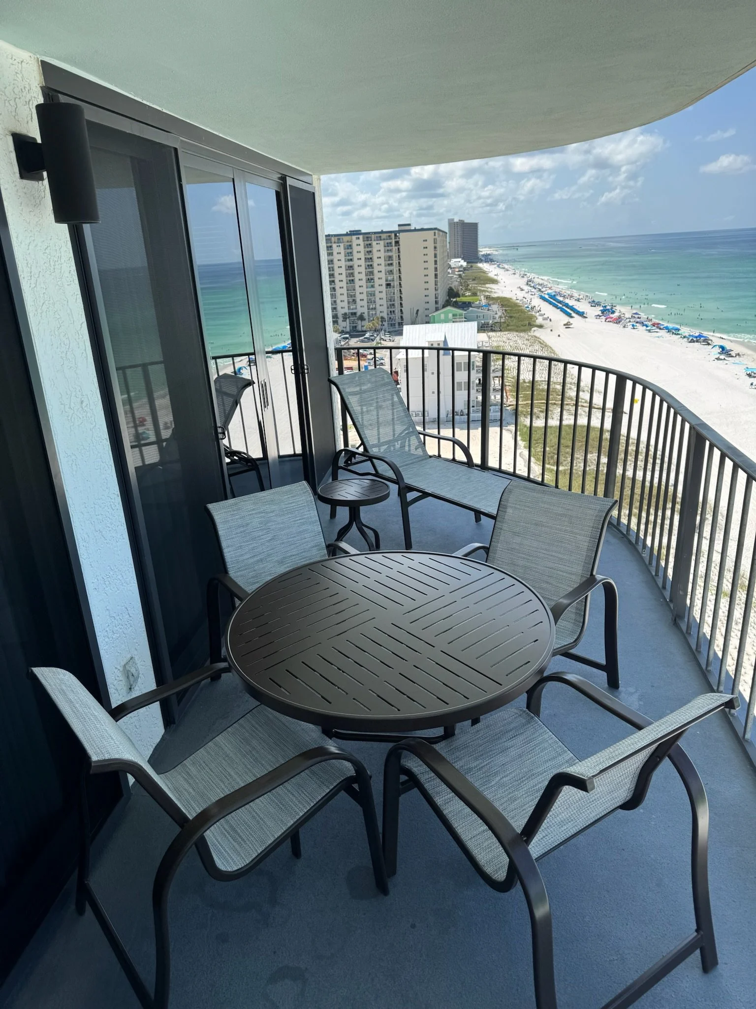 Balcony with outdoor furniture overlooking a beach with umbrellas and high-rise buildings.