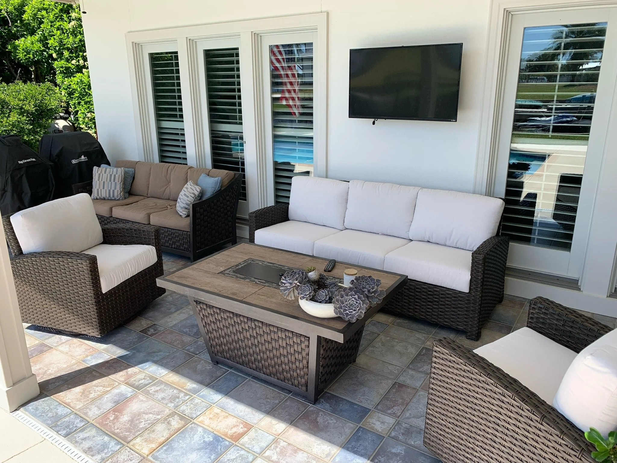 Patio with wicker and cushioned seating, a wooden coffee table with succulents, outdoor grill, sliding glass doors, and a wall-mounted TV.