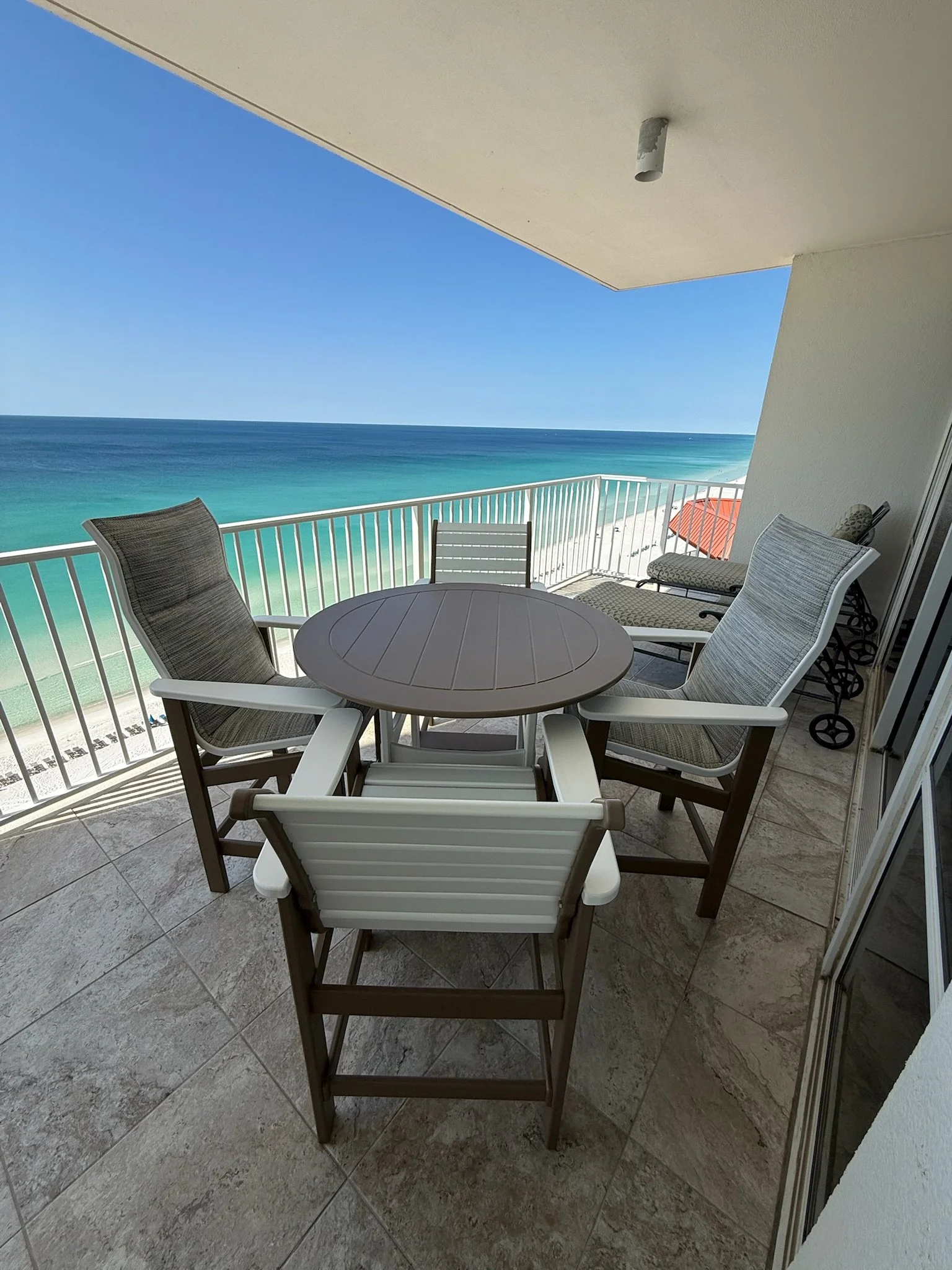 Balcony with a round table and four chairs overlooking the ocean under a blue sky.