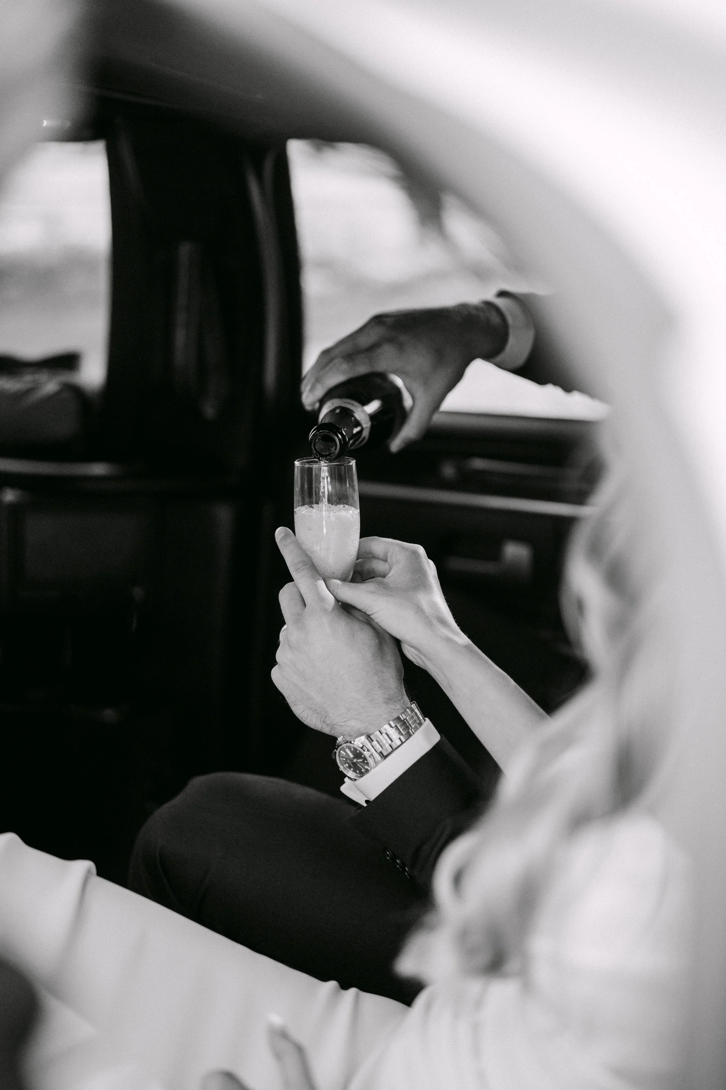 A person holding a wine glass filled with a liquid, while another person pours wine from a bottle into the glass. The scene appears to be a social or celebratory setting.