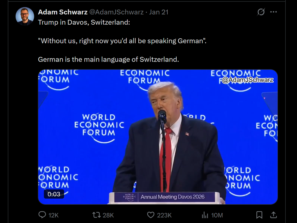 A man dressed in a dark suit, white shirt, and red tie speaking at a podium during the World Economic Forum at Davos, Switzerland, with a blue background displaying the forum's logo and event title.