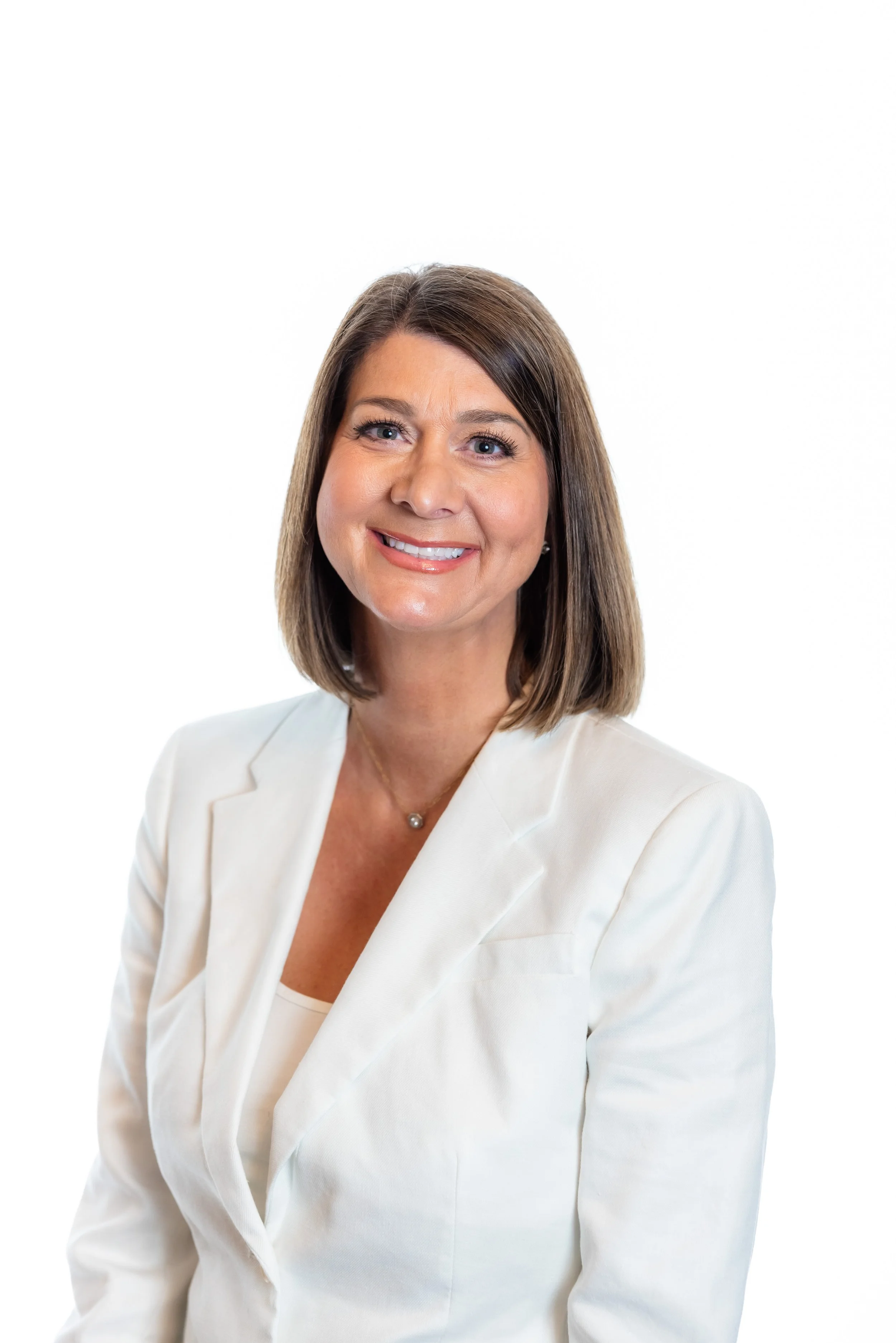 Woman with shoulder-length brown hair and wearing a white blazer smiling at camera.
