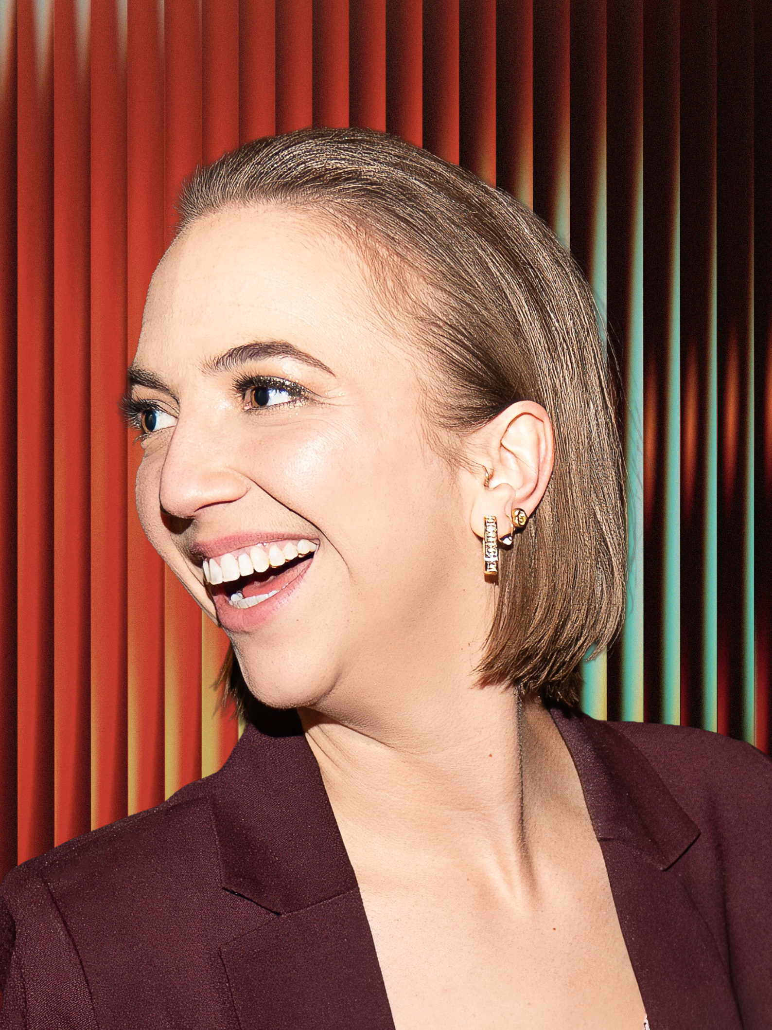 Close-up of a woman smiling with short, straight hair, wearing a dark blazer, against a colored striped background.