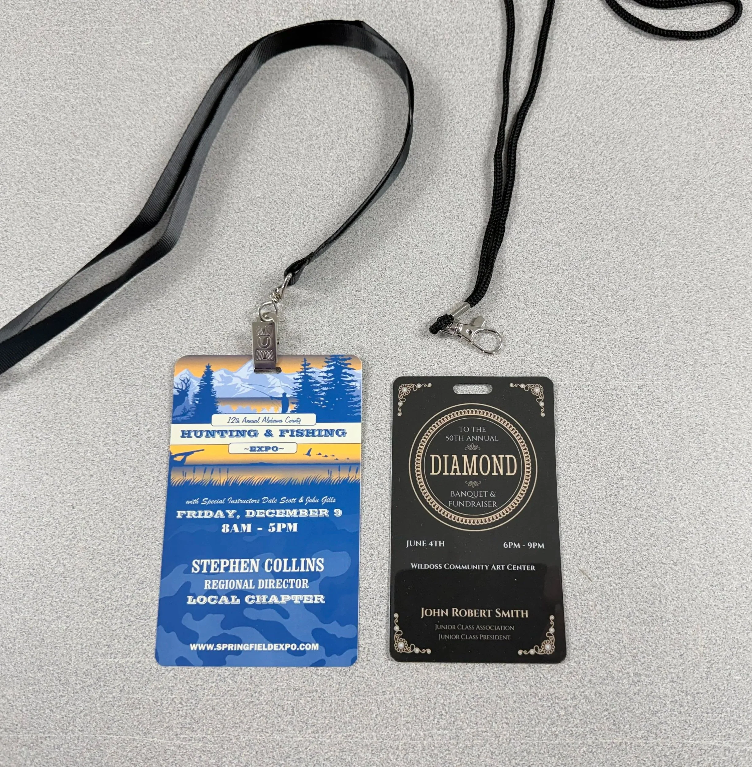 Two event badges with lanyards on a gray surface. One badge is blue and white for a hunting and fishing expo with information about the event date, location, and speaker. The other badge is black with gold details for a diamond banquet and fundraiser