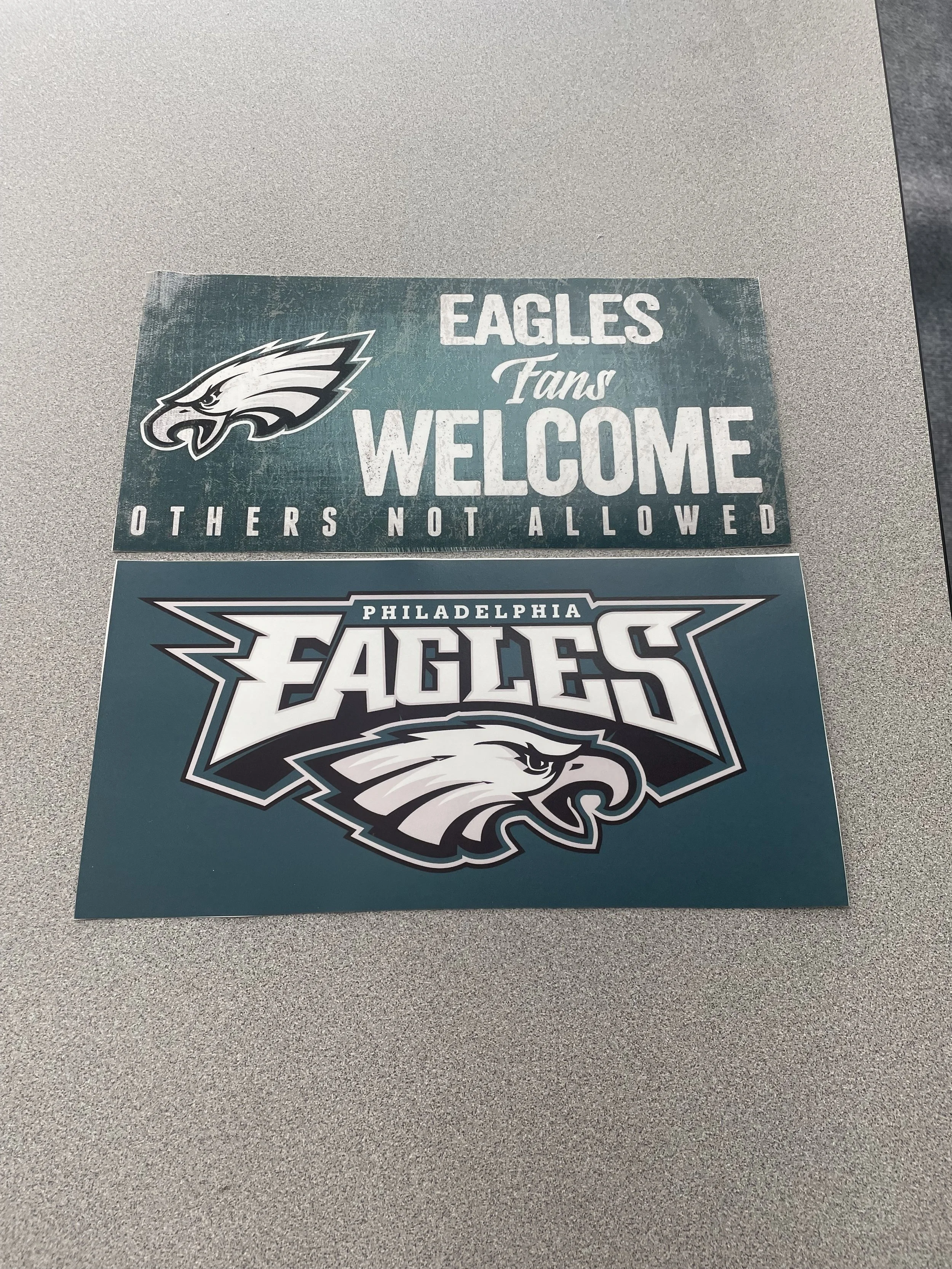 Two Philadelphia Eagles stickers, one with a logo and the other with team name and mascot, placed on a gray surface.