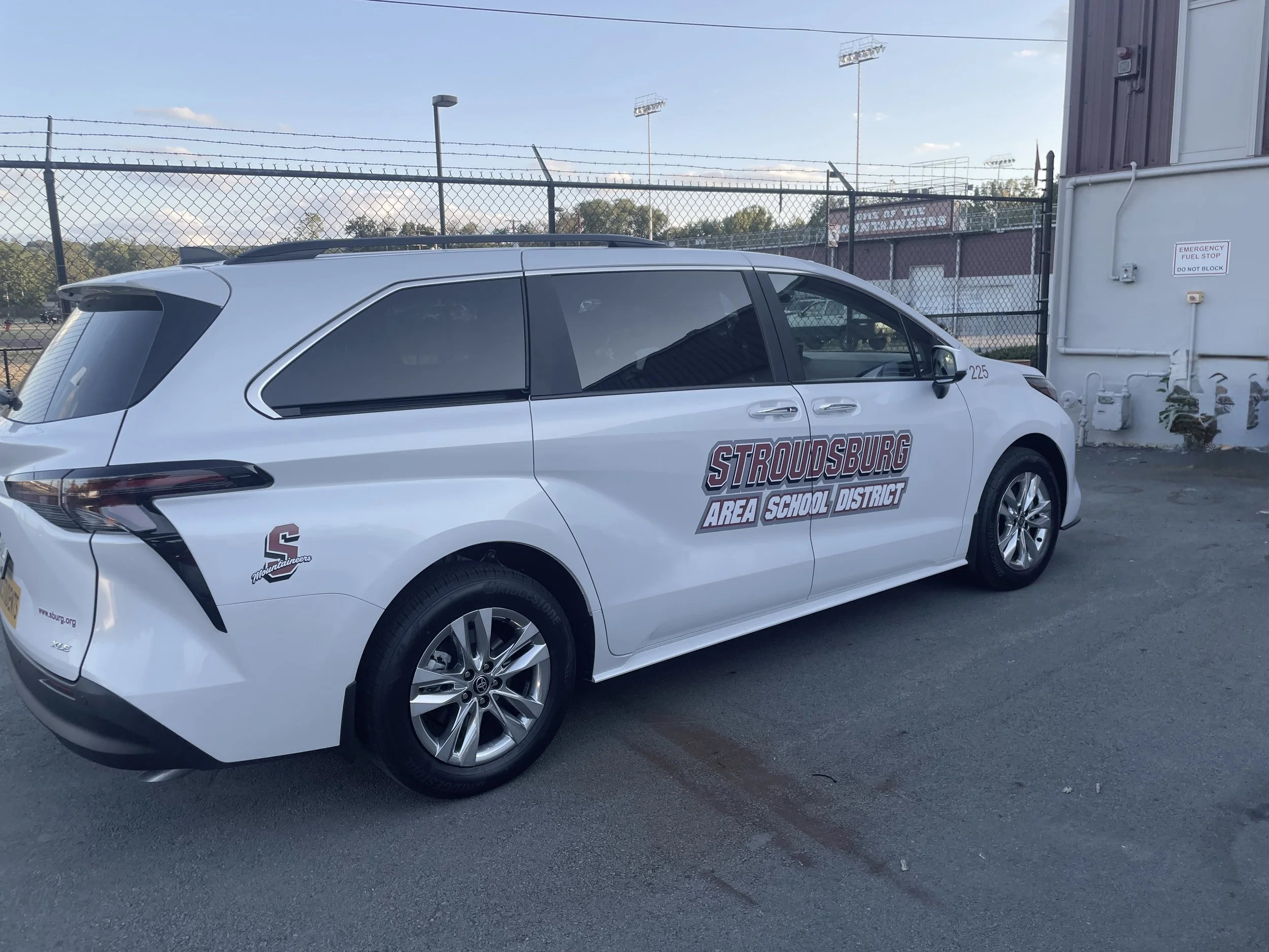 A white vehicle with 'Stroudsburg Area School District' written on the side, parked near a chain-link fence and a building.
