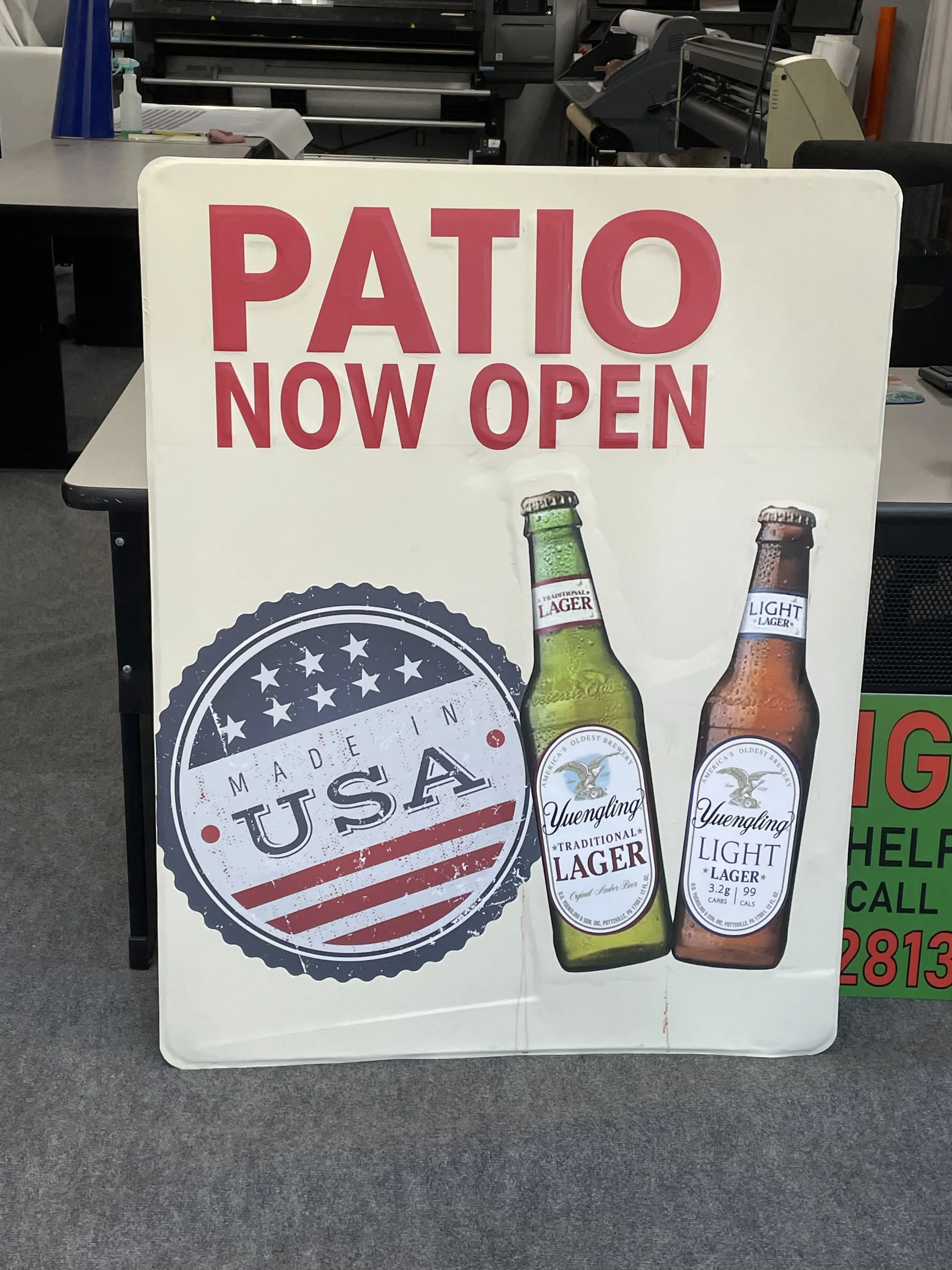 Signboard announcing 'Patio Now Open' with a logo 'Made in USA' and pictures of Yuengling traditional lager and light lager bottles.