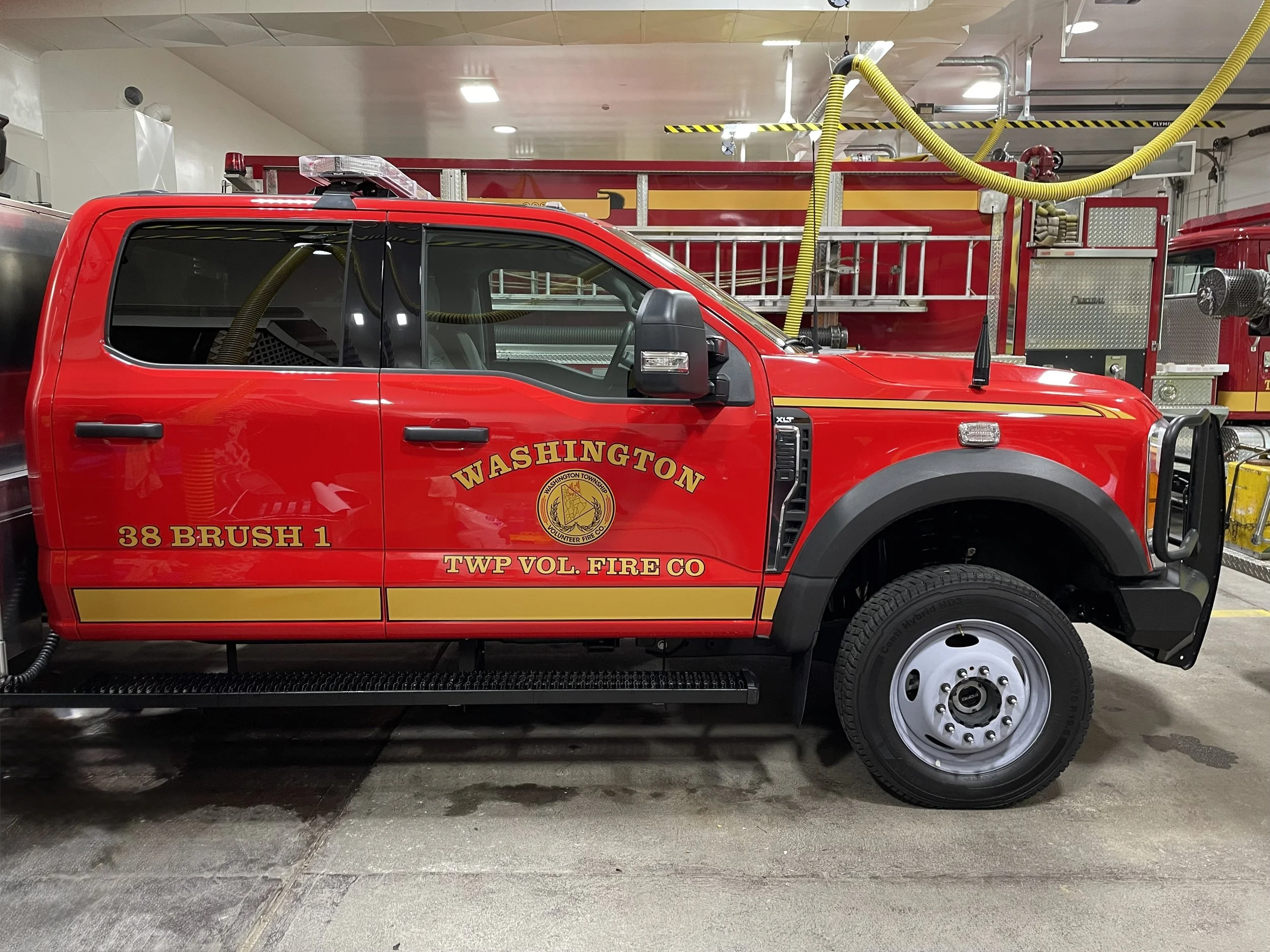Red fire rescue truck inside fire station with yellow hoses and firefighting equipment.