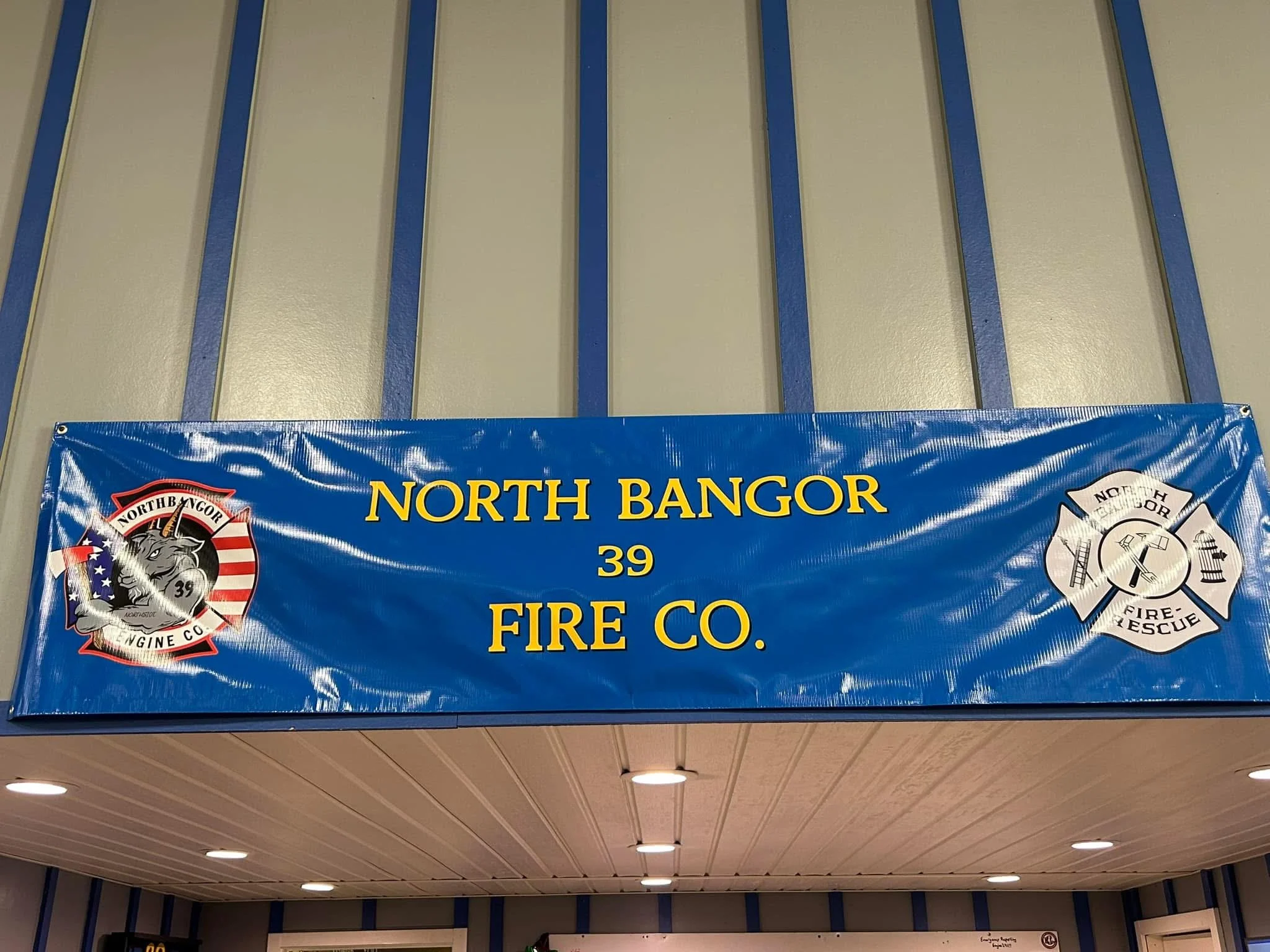 Blue sign with yellow text reading 'North Bangor 39 Fire Co.' and fire department logos on either side, mounted on a wall.