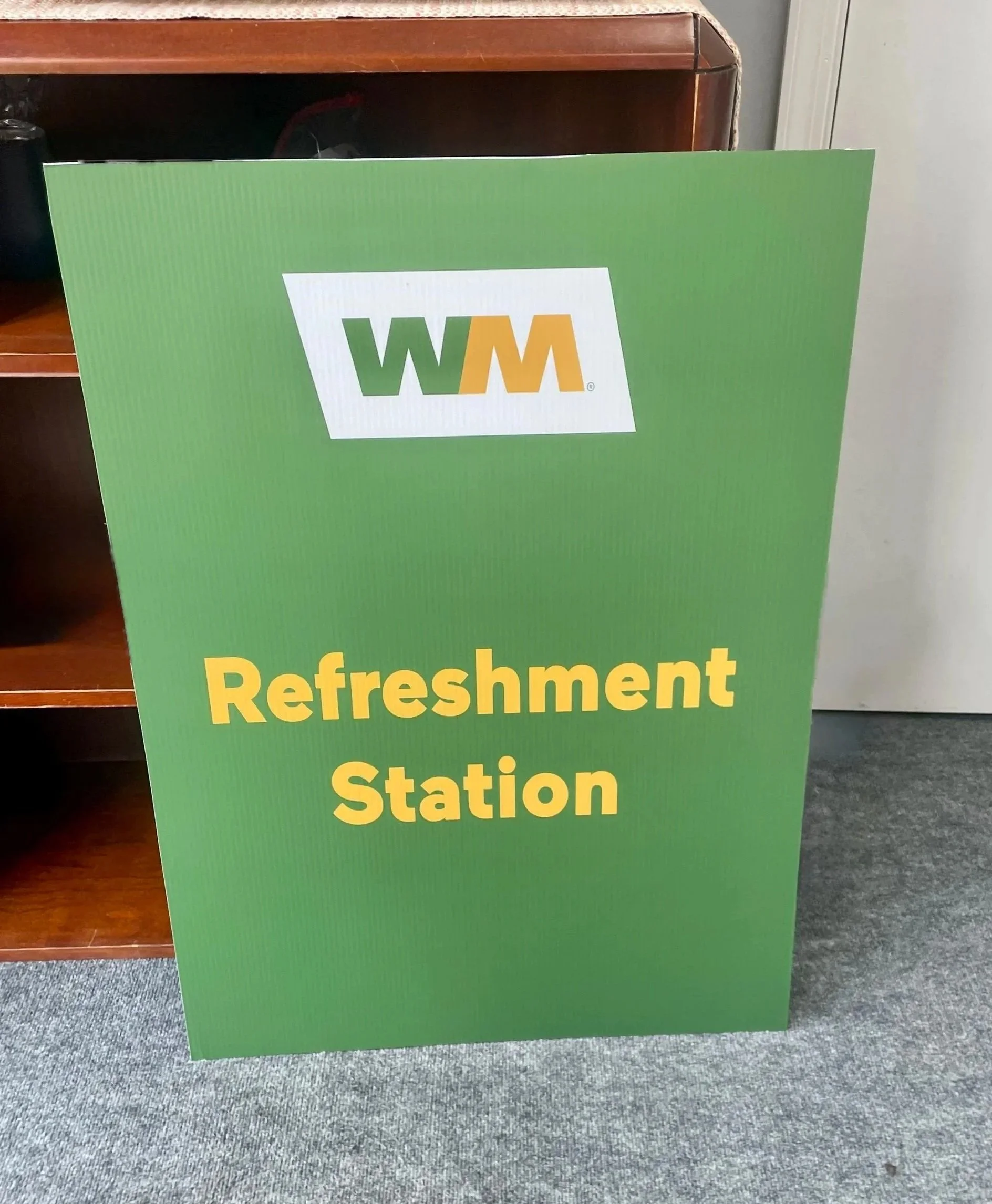 A green sign with the WM logo at the top and yellow text that reads 'Refreshment Station.'