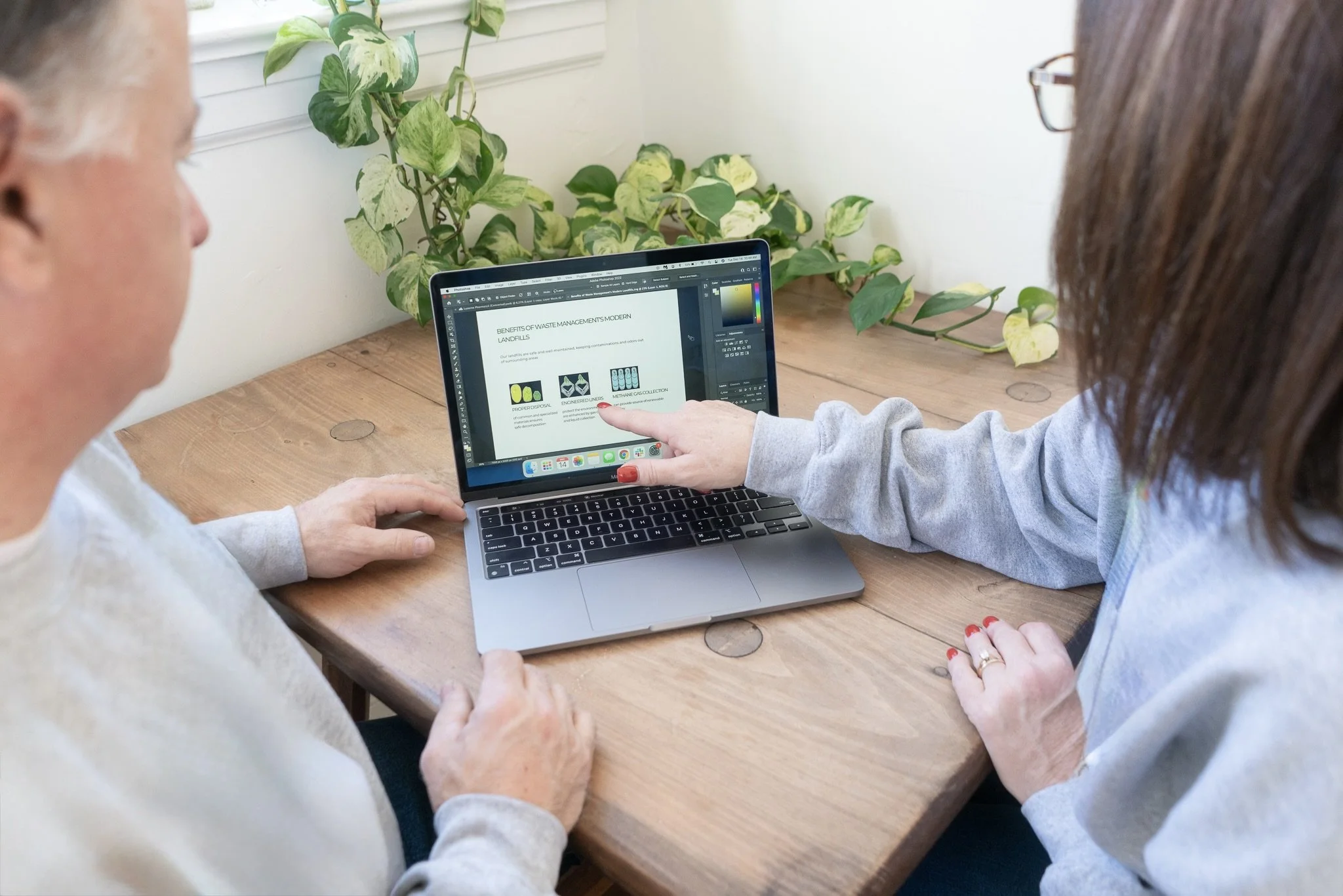 Two women looking at a laptop screen displaying a presentation slide about waste management benefits, one woman is pointing at the screen.