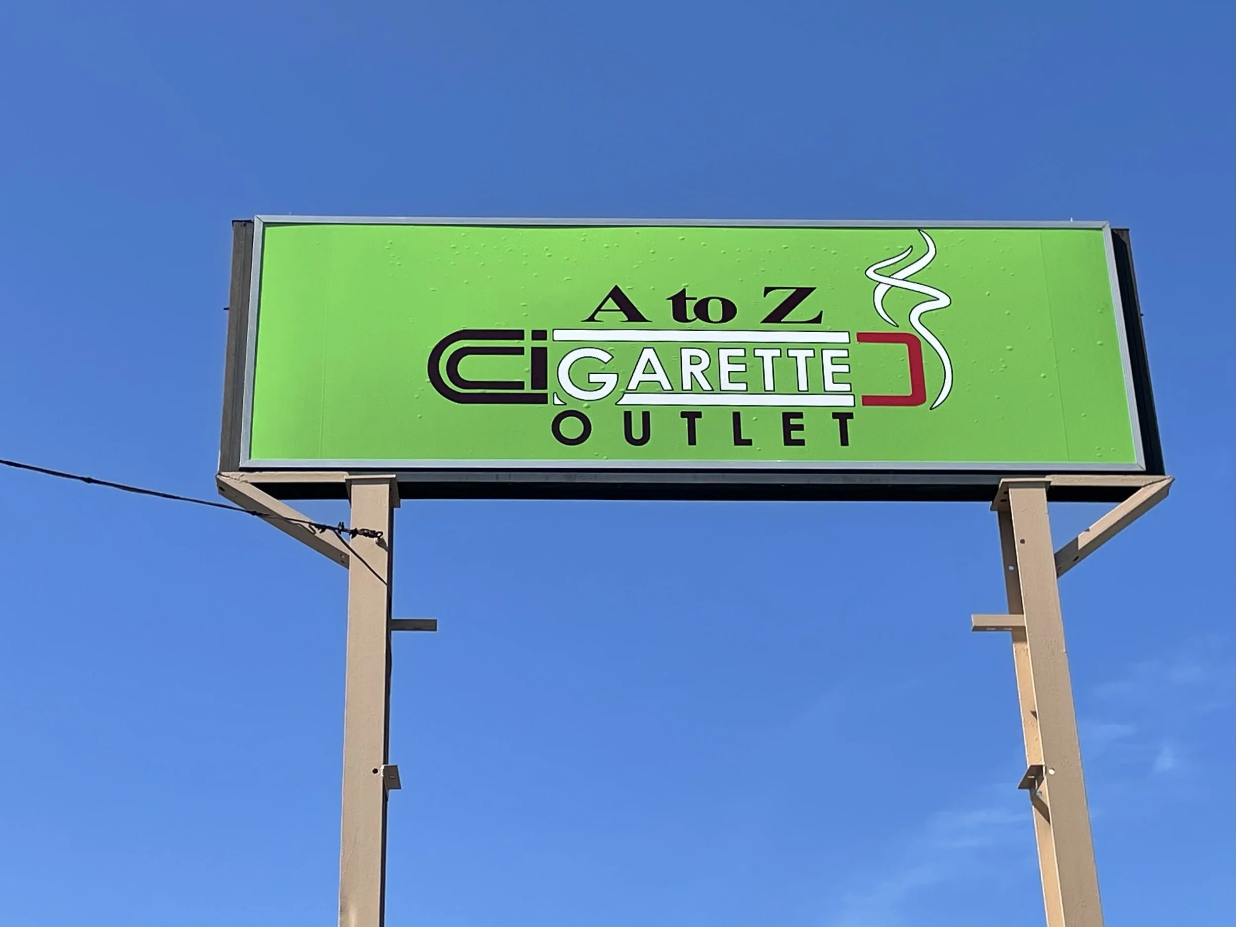 A bright green outdoor sign for an outlet store called 'A to Z Cigarette Outlet' with a stylized cigarette graphic and the words 'GARETTE' in the center.