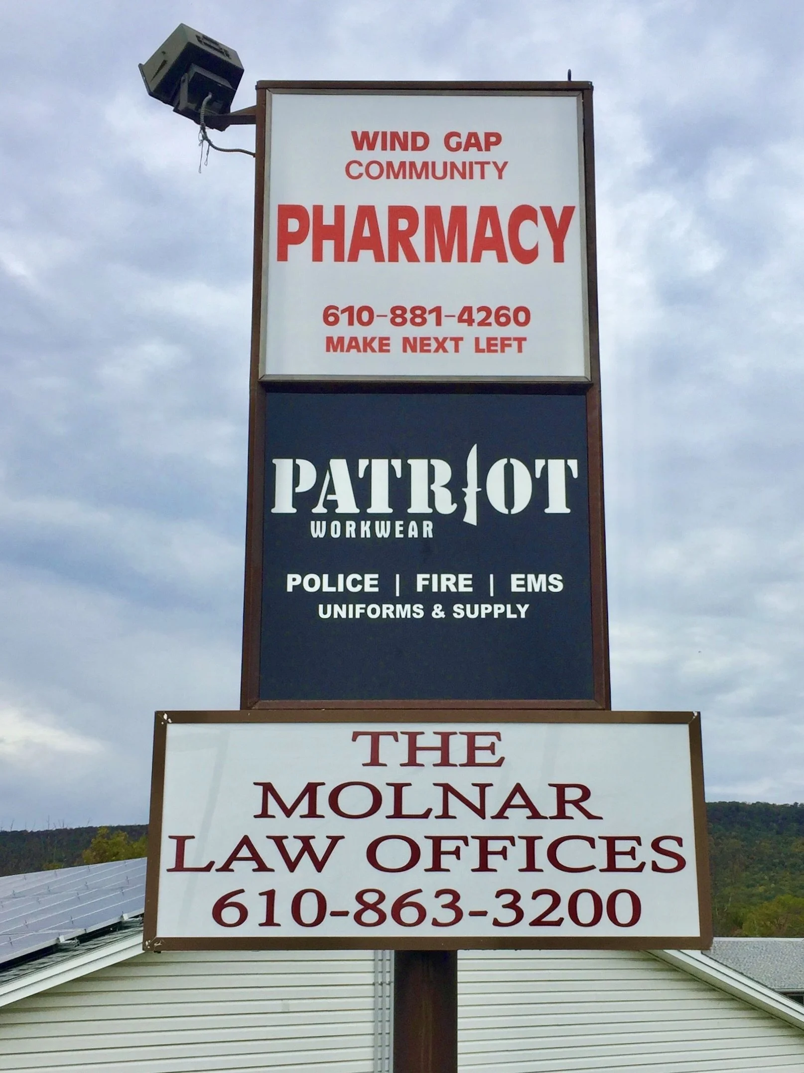 Sign for Wind Gap Community Pharmacy with phone number and directions, advertising Patriot workwear for police, fire, and EMS uniforms and supplies, and for Molnar Law Offices with phone number.