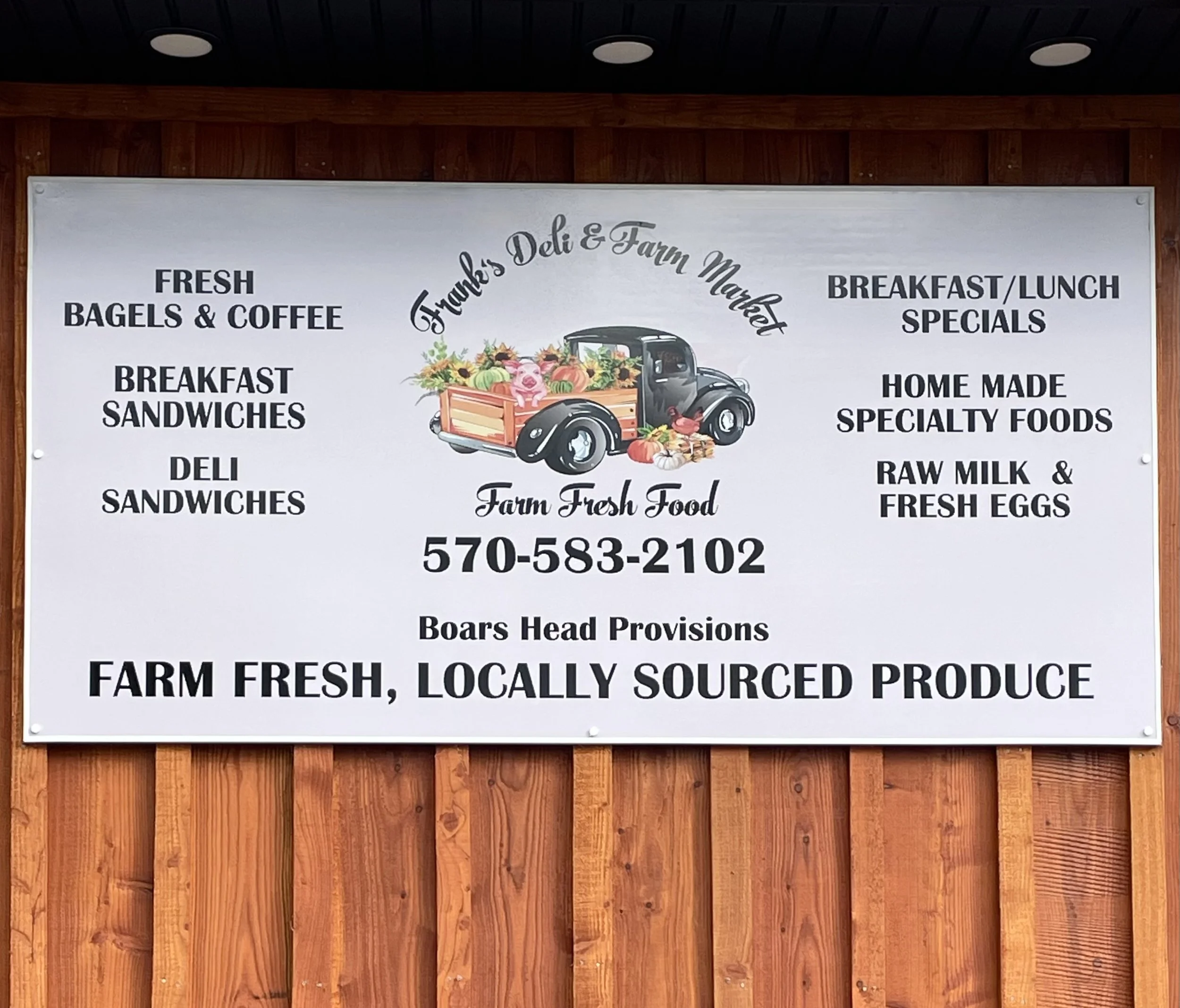 Signboard for Thanks Deli & Farm Market featuring a vintage truck filled with farm produce, with menu items listed including fresh bagels and coffee, breakfast and deli sandwiches, homemade specialty foods, raw milk and eggs, and farm fresh, locally 