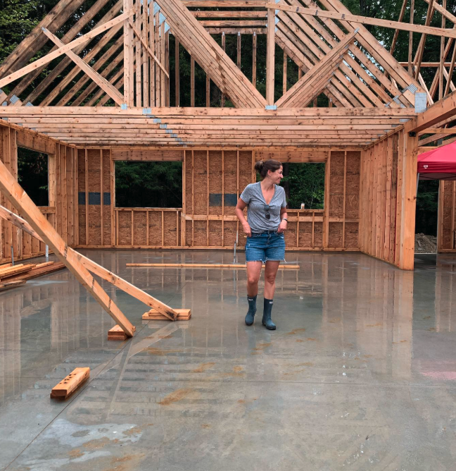 A woman walking in the foundation of a house under construction, with wooden framing and a concrete floor.