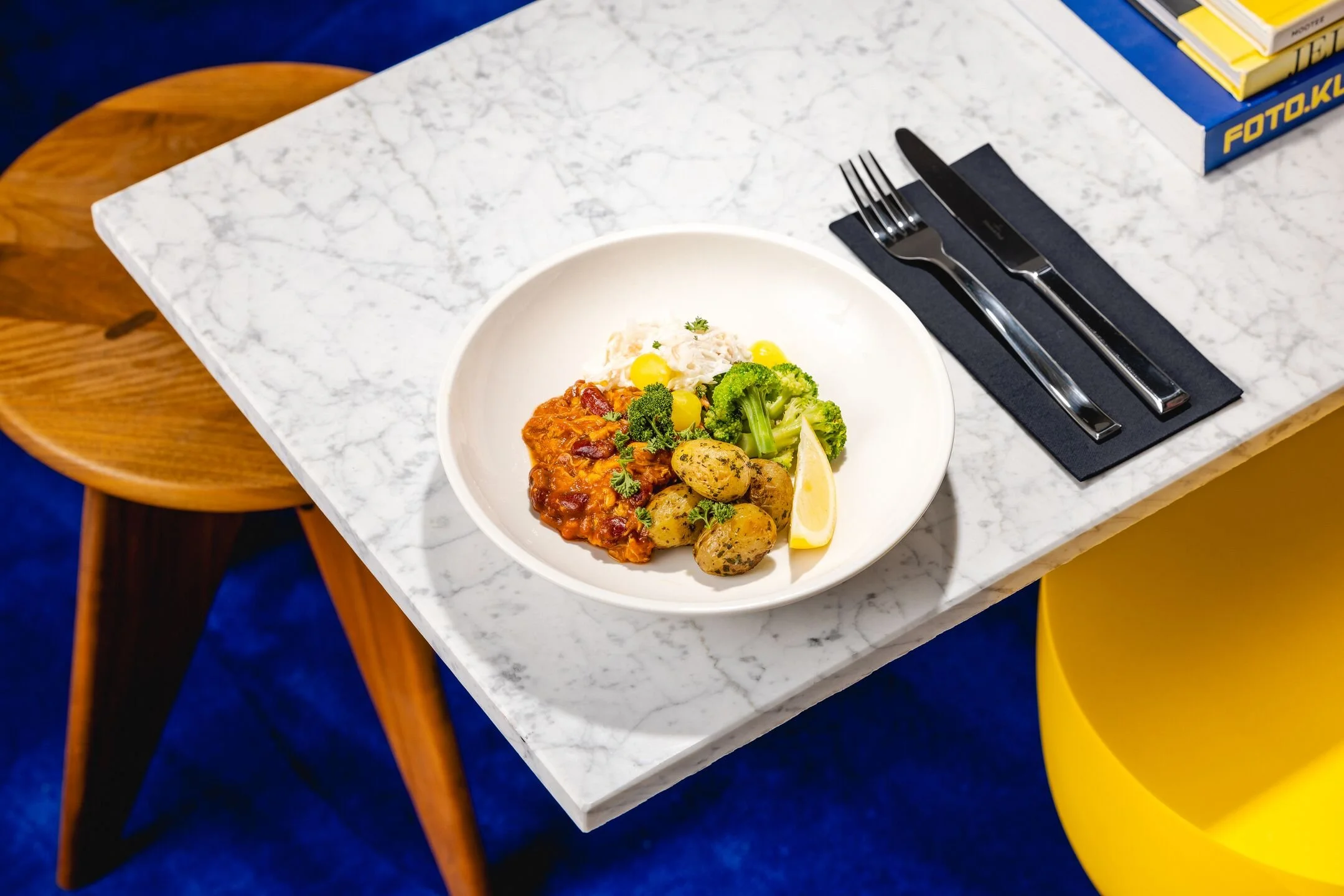 Plate with rice, green broccoli, boiled potatoes, tomato-based stew, and lemon wedge on a white marble table.