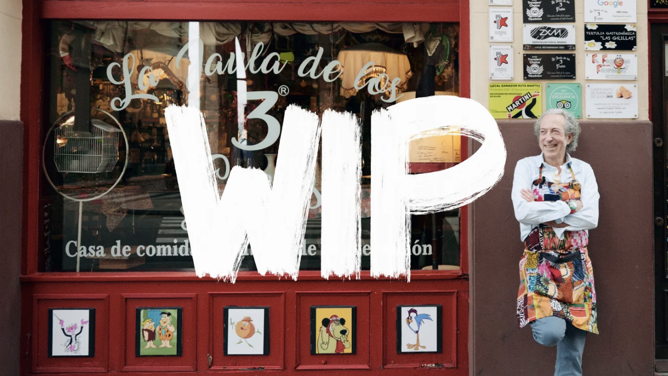 A person standing outside a restaurant named 'La Tabla de los 3WIP' with a colorful apron, smiling with arms crossed.