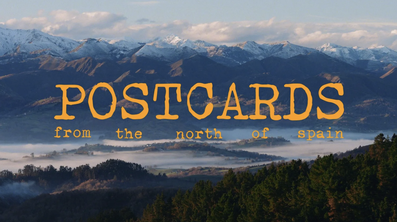 A scenic landscape of mountains with snow caps, rolling hills, and a forest under a cloudy sky, overlaid with the text 'Postcards from the north of Spain' in orange font.
